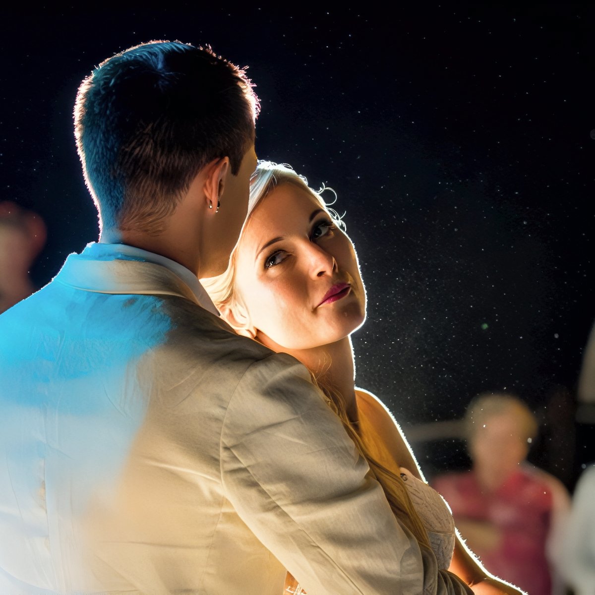 At their destination wedding, the bride and groom share a romantic dance, gently illuminated by soft lighting that stands out against the dark background.