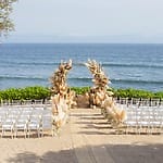 White chairs and a pampas grass arch arranged for a destination wedding ceremony on the oceanfront.