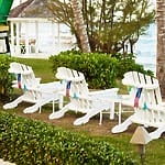 Three white Adirondack chairs face the ocean, near trees and popular destination wedding attractions in Jamaica.