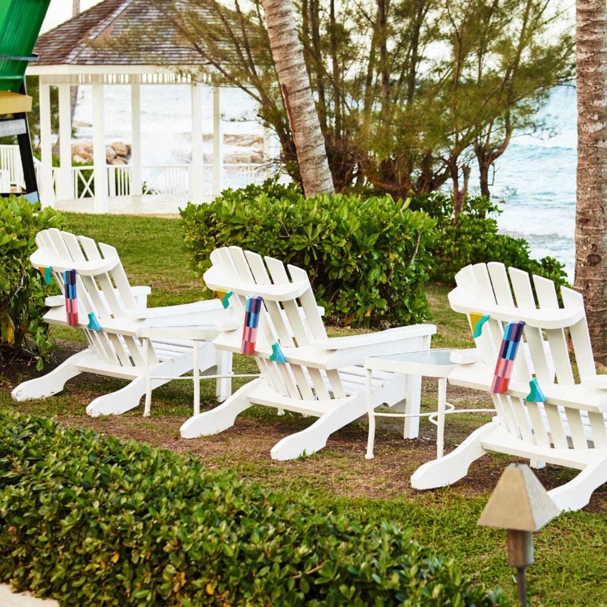 Three white Adirondack chairs face the ocean, near trees and popular destination wedding attractions in Jamaica.
