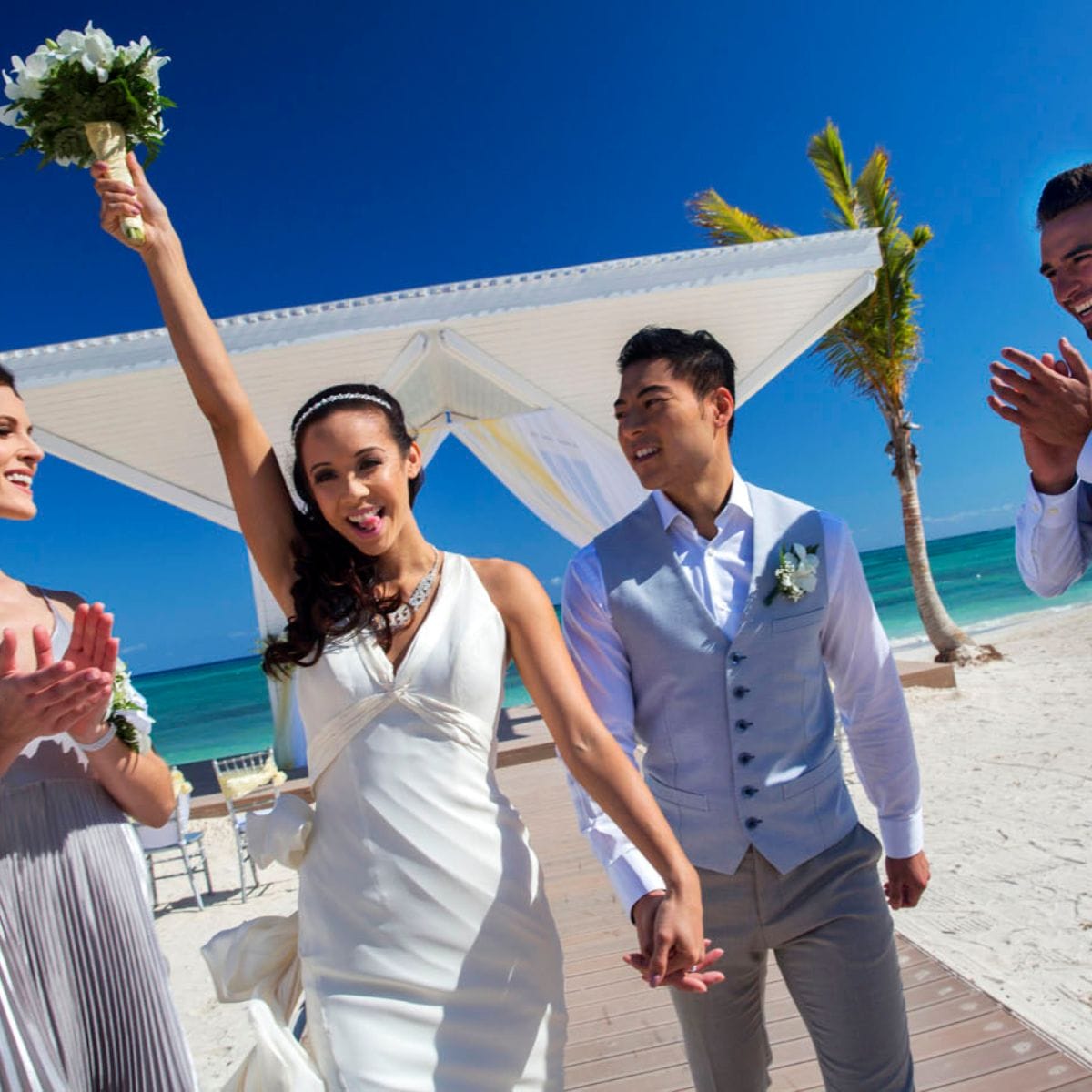 Bride holding bouquet, smiling with groom and friends at a stunning Jamaica destination wedding.