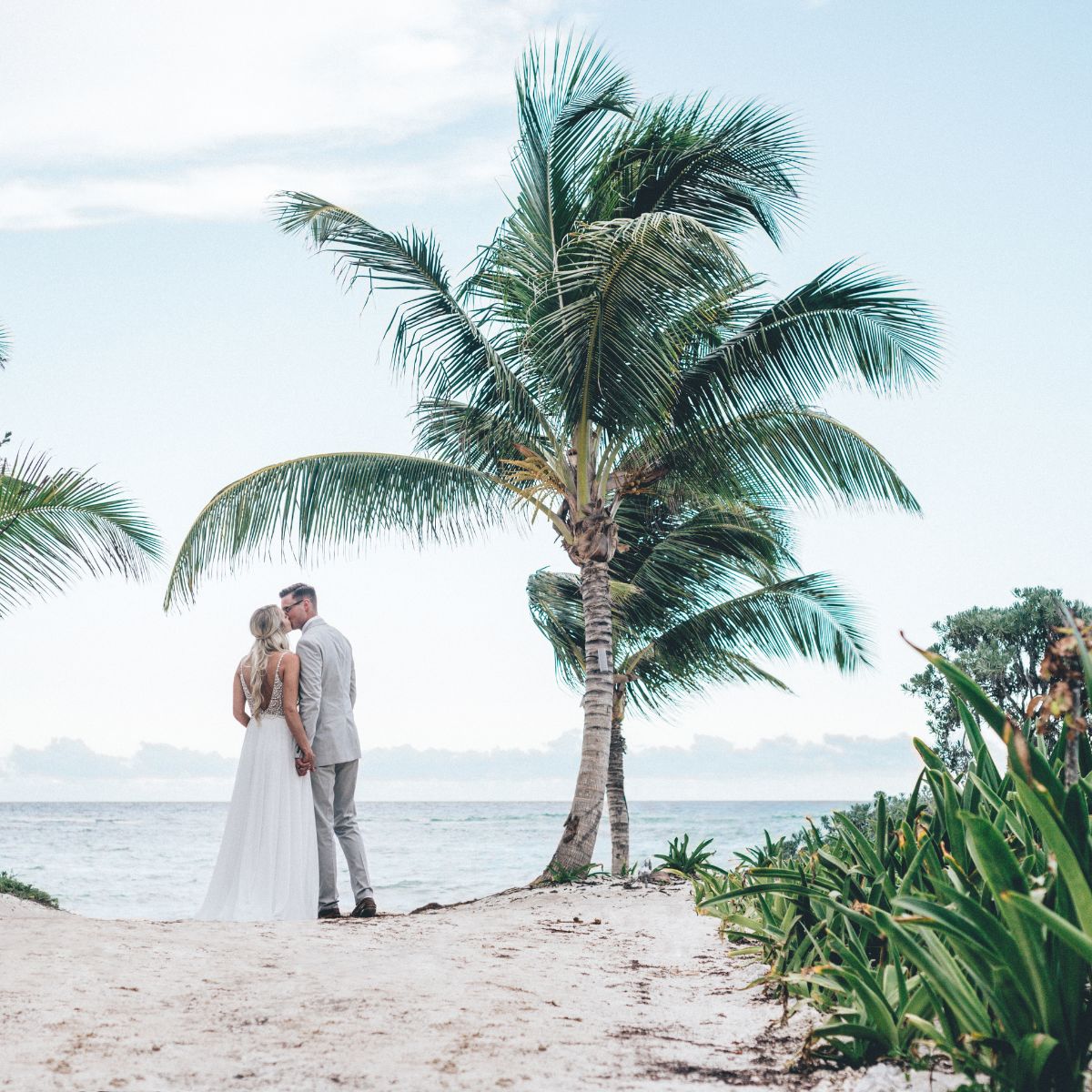 A couple in wedding attire stands on a sandy path at one of Tulum’s top destination wedding locations.