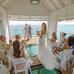 A bride stands and smiles at guests during a beautifully orchestrated wedding ceremony inside a small overwater pavilion with clear ocean views, embracing the charm of free weddings.
