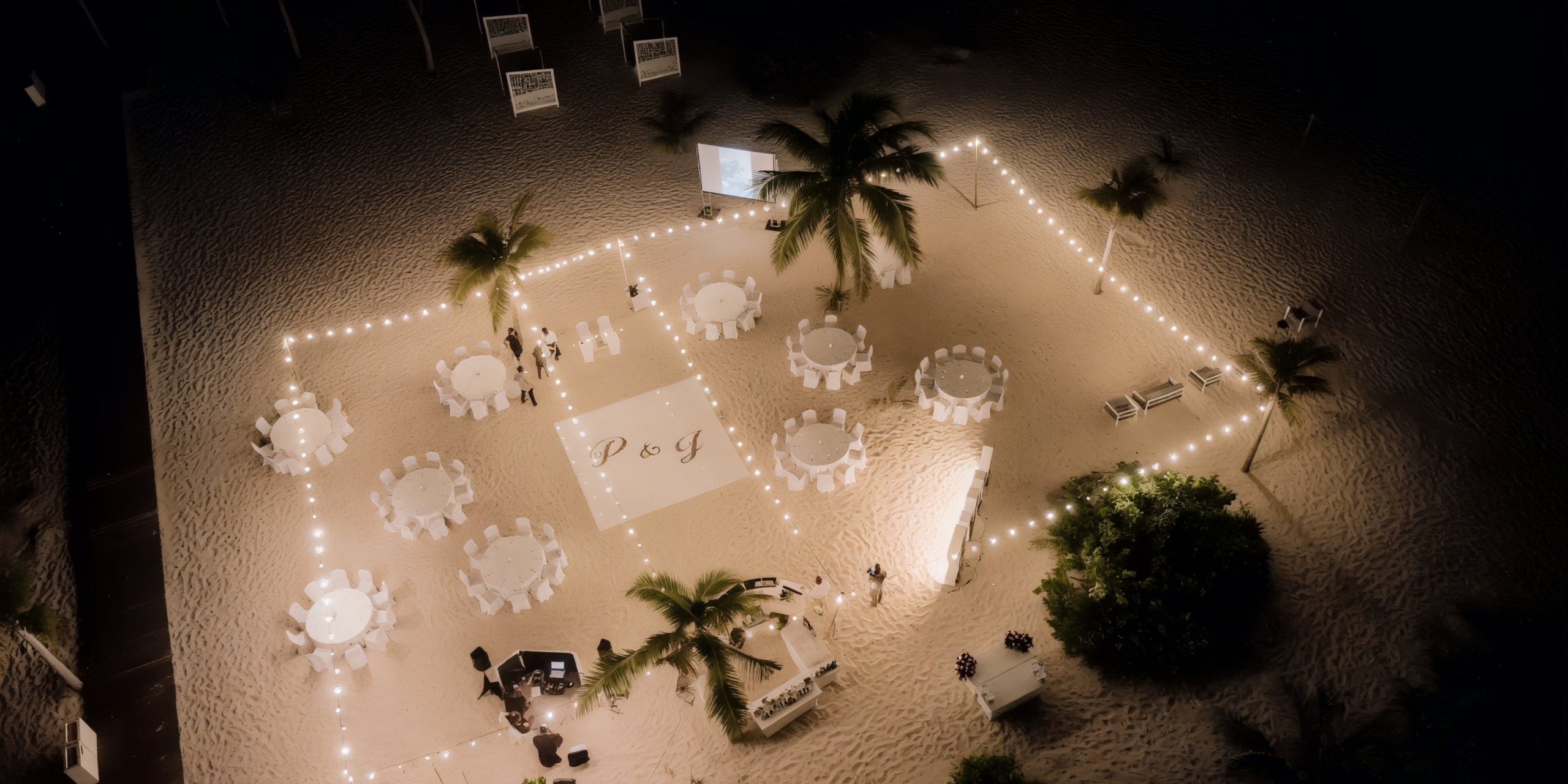 Aerial view of a destination wedding setup at Majestic Elegance Costa Mujeres lit by string lights at night.