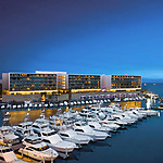 A destination wedding venue at dusk with luxury yachts parked in the water in front of Breathless Cabo San Lucas Resort and Spa lit up against the evening sky.