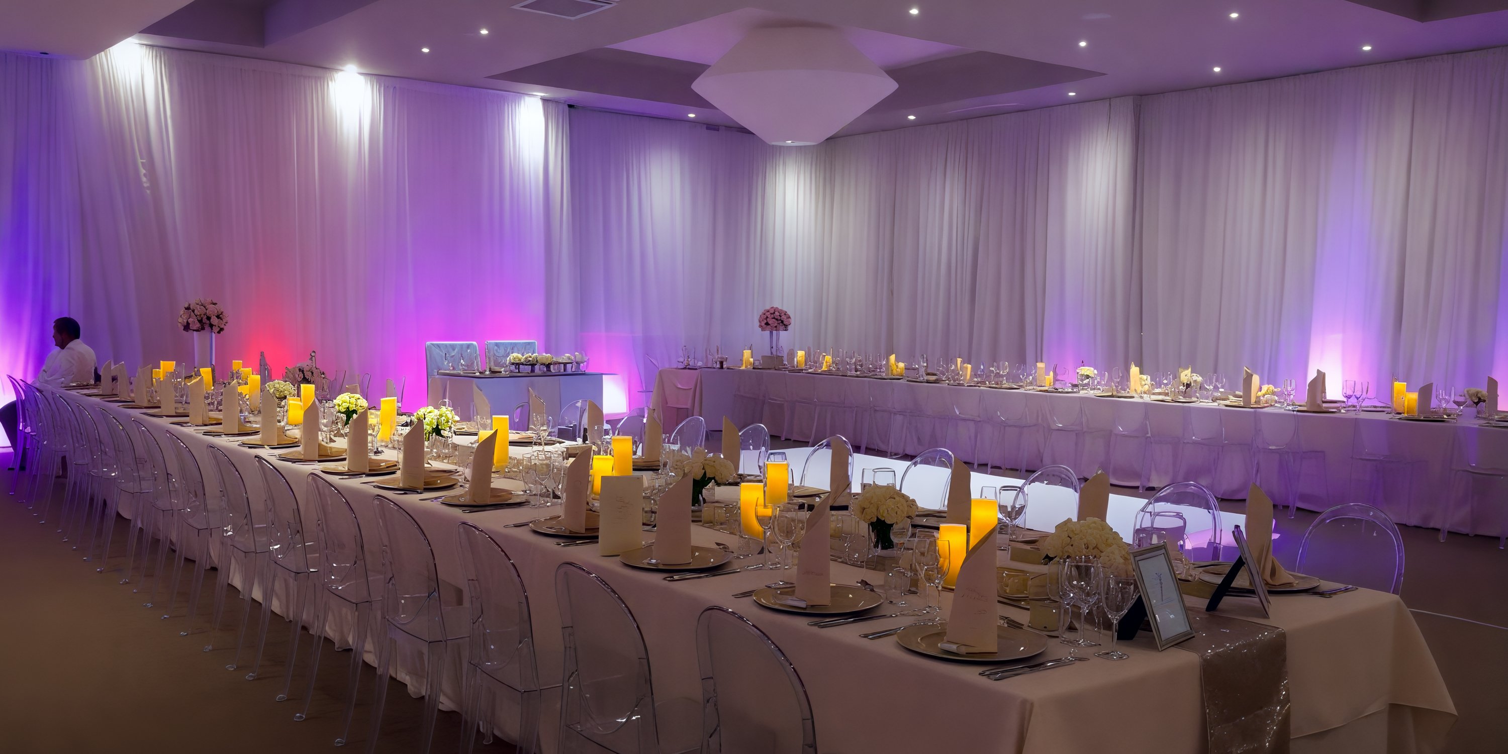Breathless Punta Cana provides an exquisite banquet hall perfect for a destination wedding, featuring tables adorned with white chairs and illuminated by soft purple lighting.