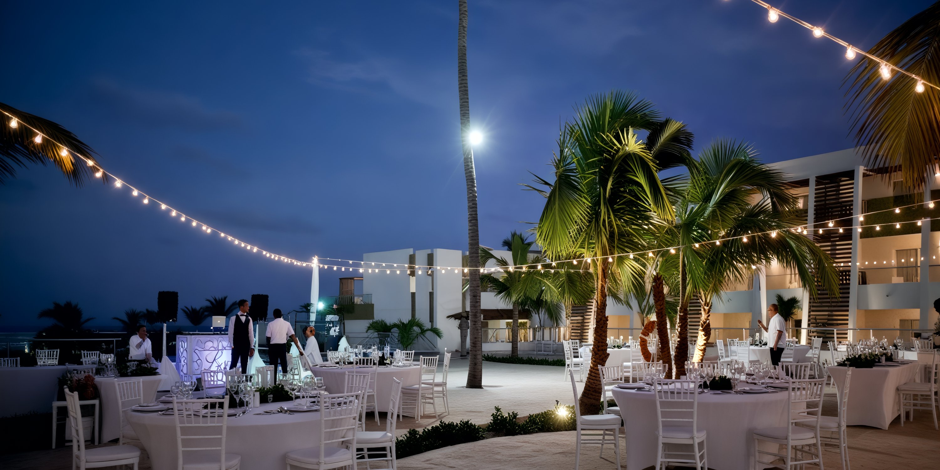 The evening wedding setup at Breathless Punta Cana Resort features elegantly arranged tables, enchanting string lights, and swaying palm trees—perfect for a destination wedding.