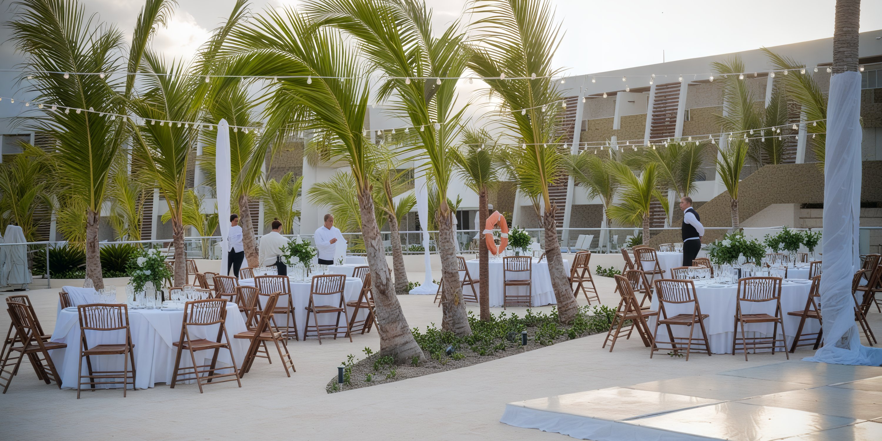 Breathless Punta Cana offers a picturesque courtyard setup for destination weddings, featuring round tables, chairs, and beautiful palm trees.