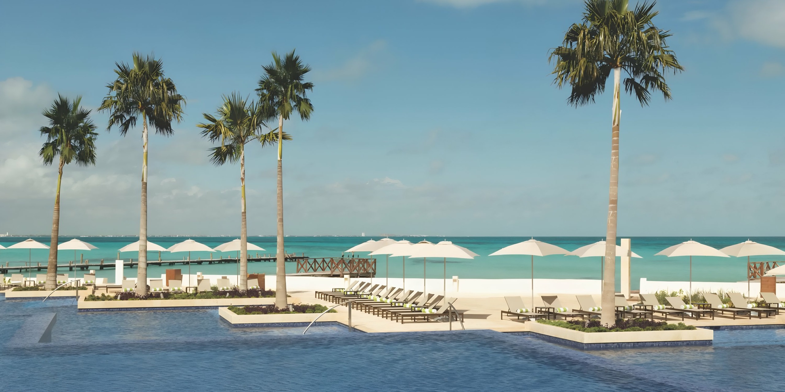 Hyatt Ziva Cancun poolside with palm trees, umbrellas, and loungers facing a calm ocean.