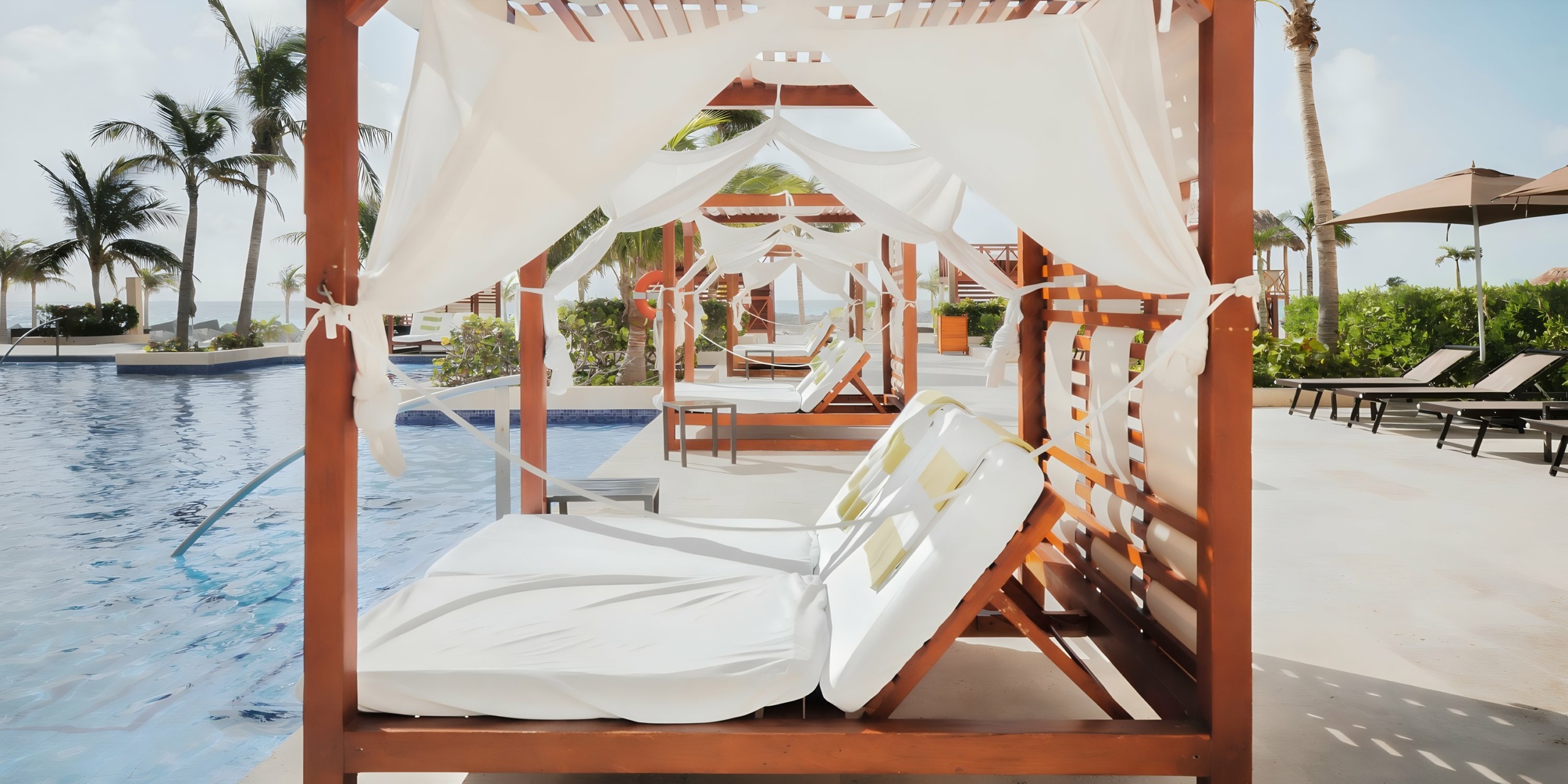 Hyatt Ziva Cancun with white curtains beside a resort pool with loungers and palm trees in the background.