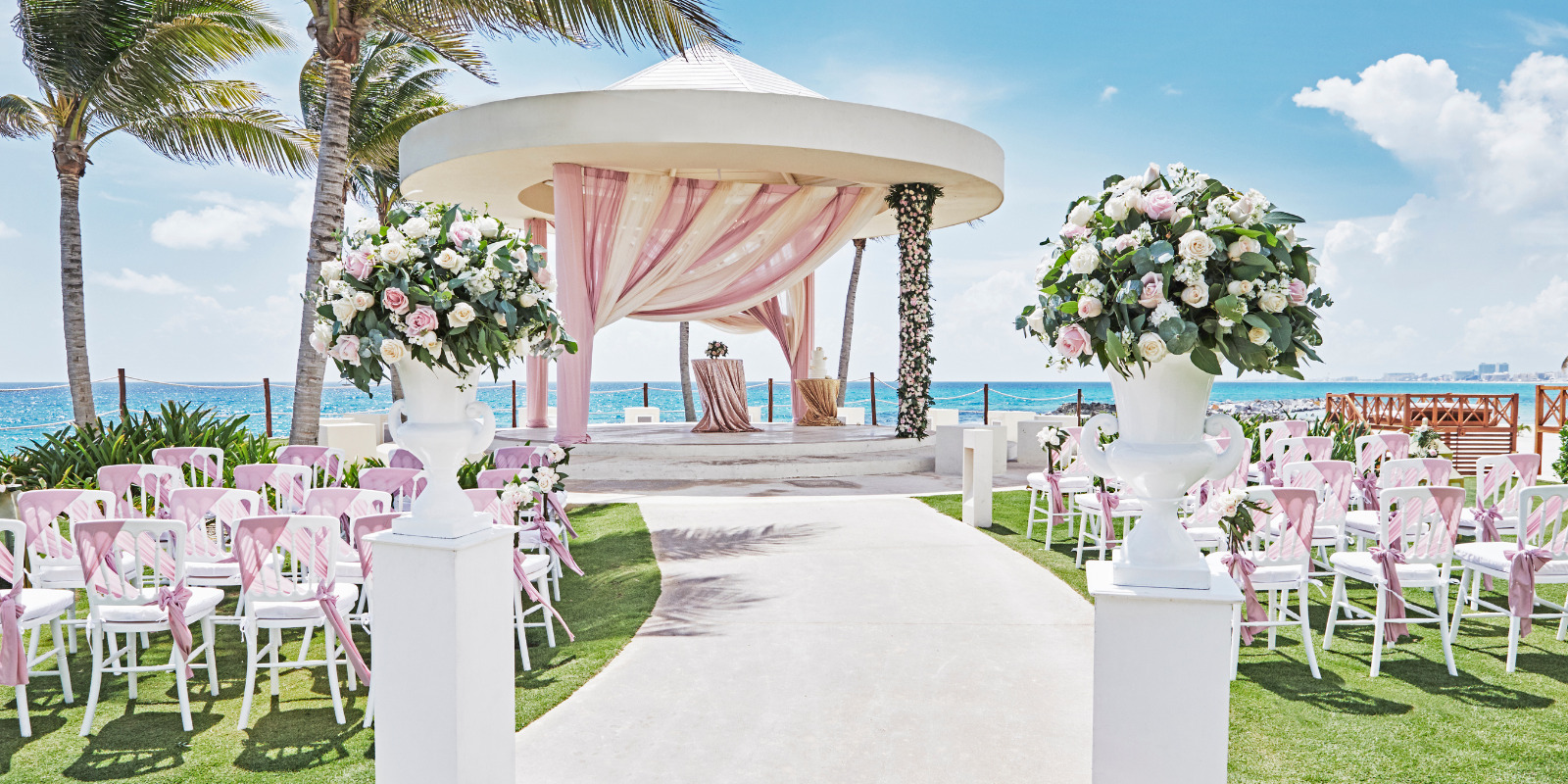 A Hyatt Ziva Cancun destination wedding ceremony set up on the beach with pink chairs.