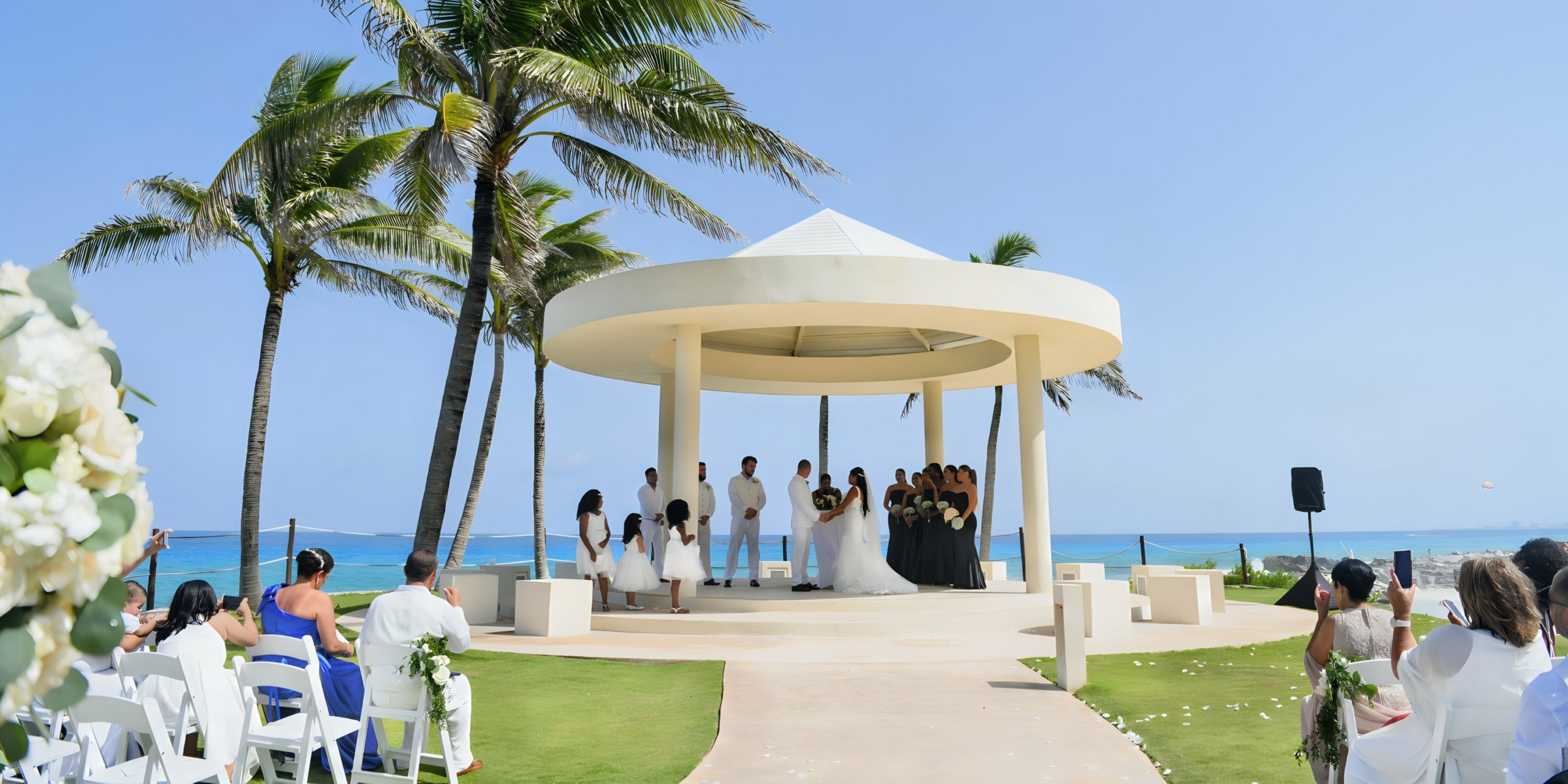 Hyatt Ziva Cancun wedding ceremony with guests seated and a couple exchanging vows under a white gazebo.