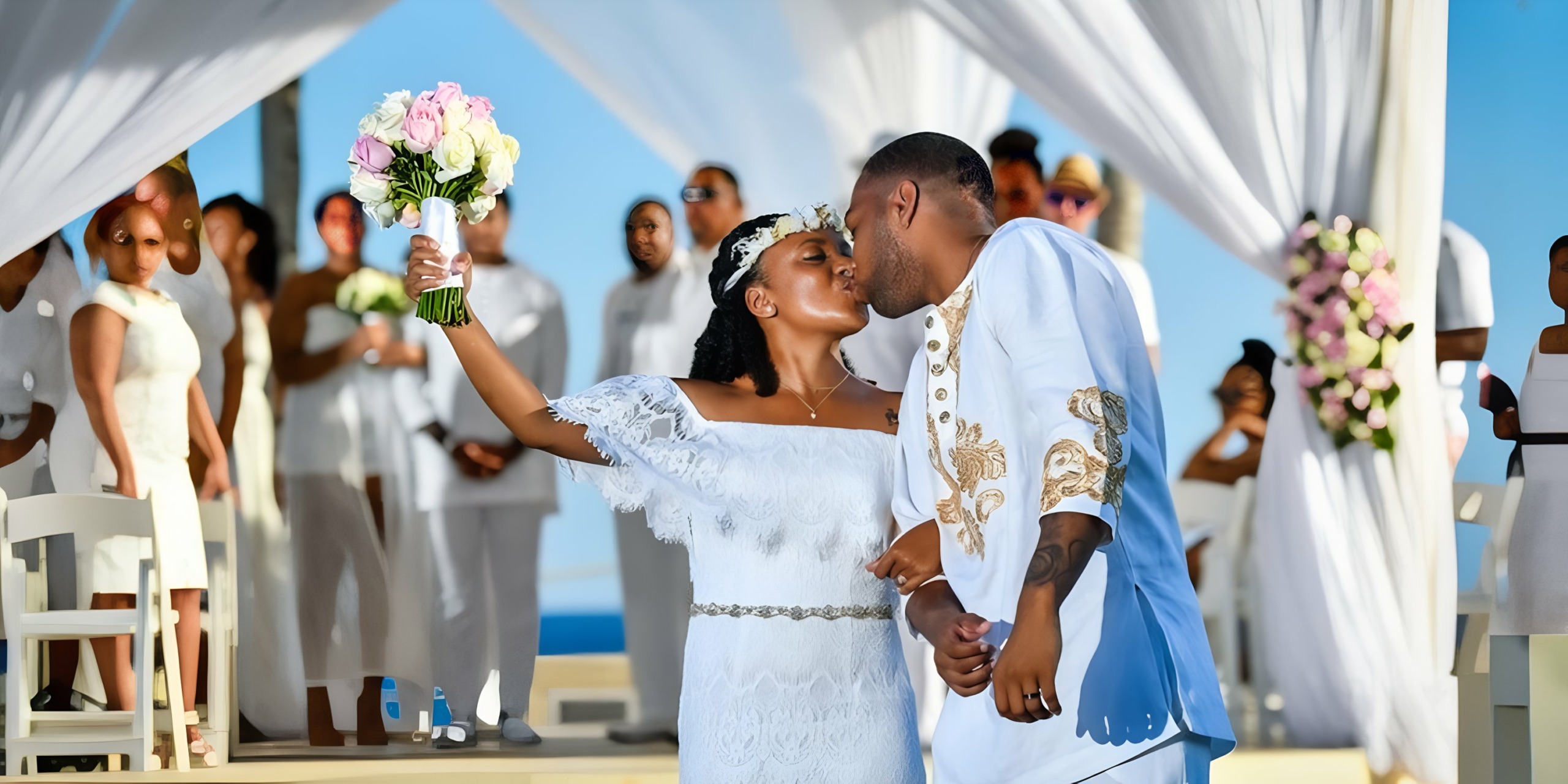 A couple exchanges a kiss under a Hyatt Ziva Cancun during a wedding ceremony by the sea, with guests dressed in white looking on.