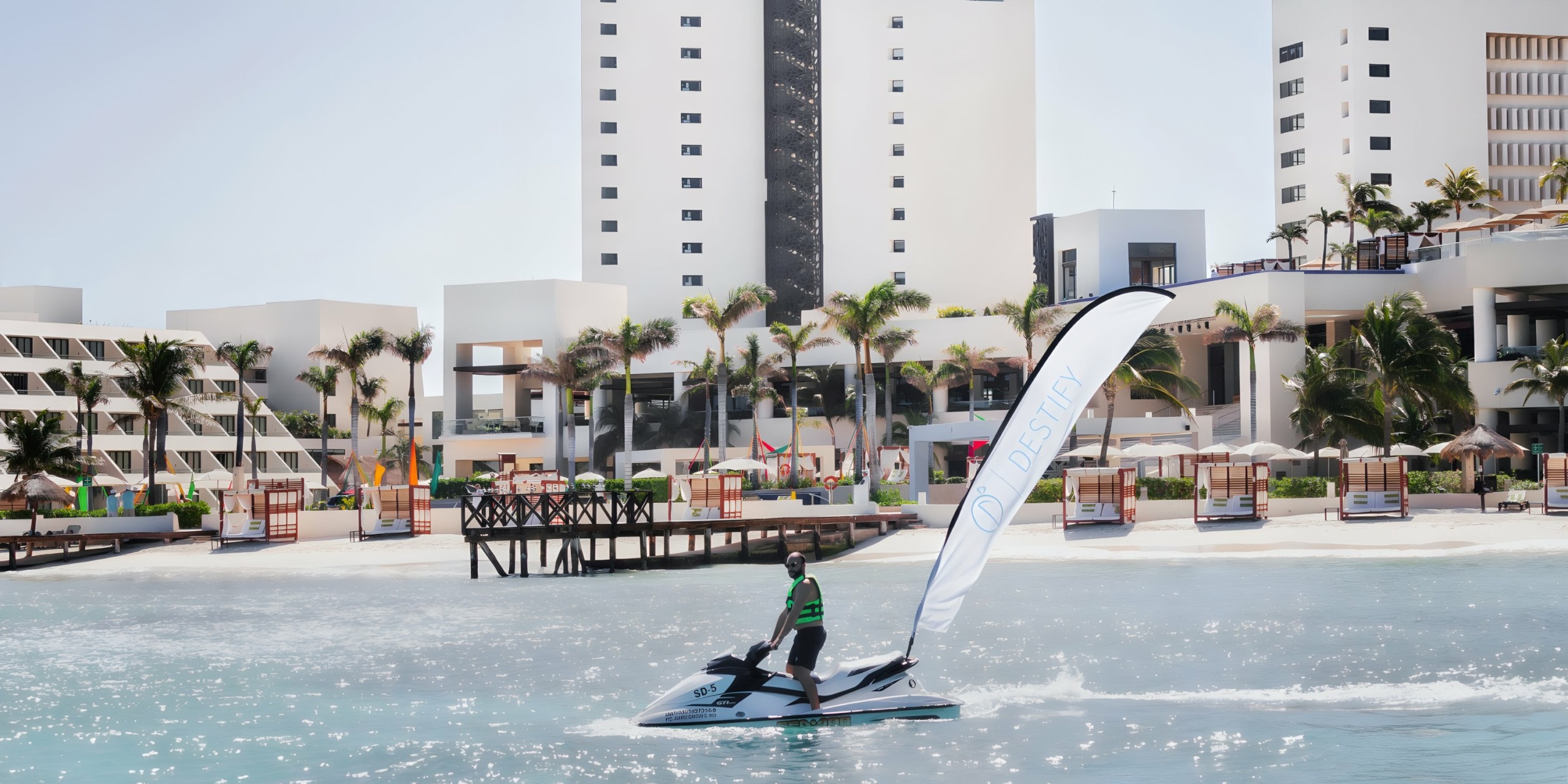 A person riding a personal watercraft near the Hyatt Ziva Cancun with modern buildings in the background.