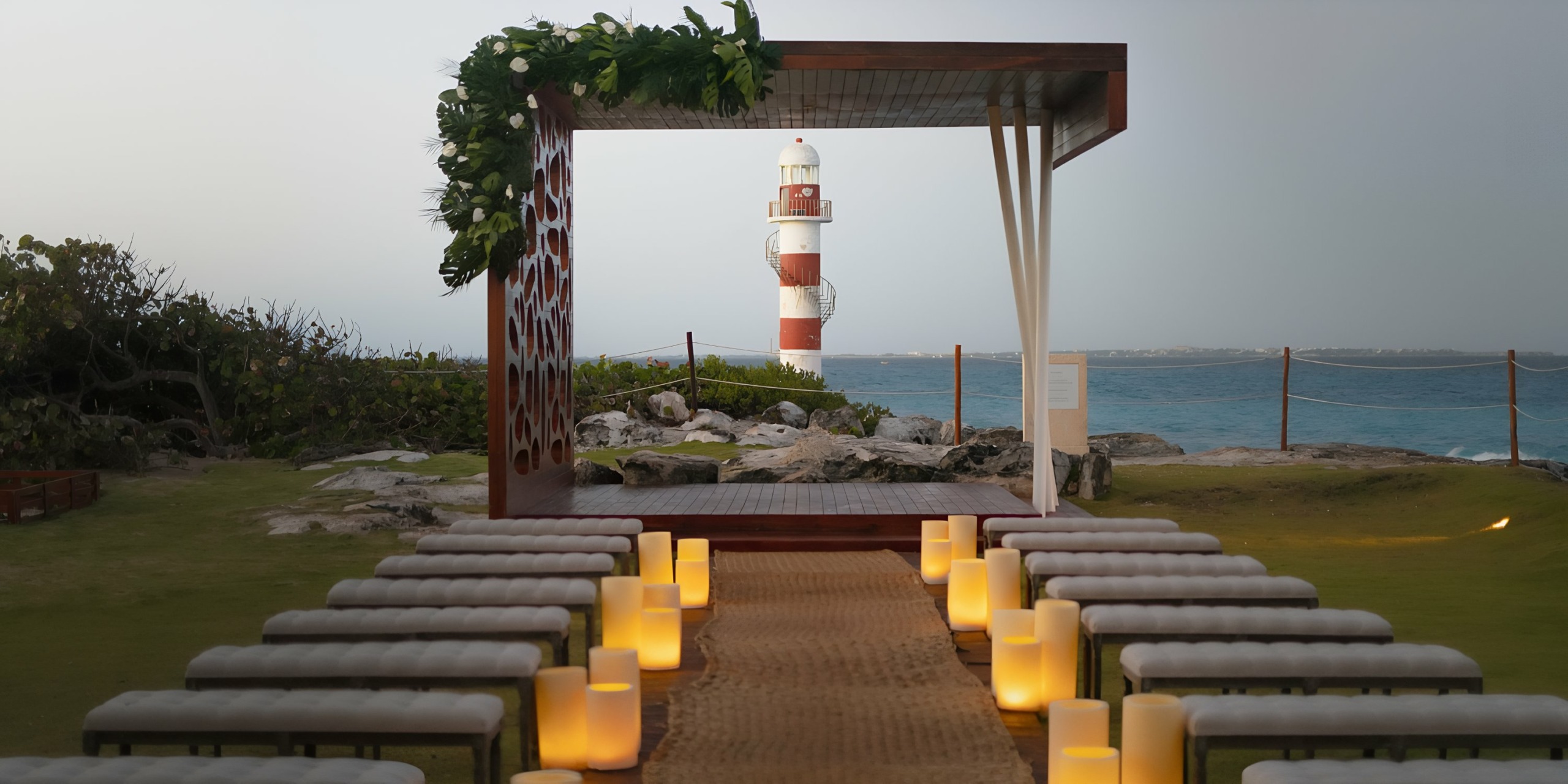 Hyatt Ziva Cancun ceremony setup on a coastal venue with an aisle lined by candles leading towards a lighthouse.
