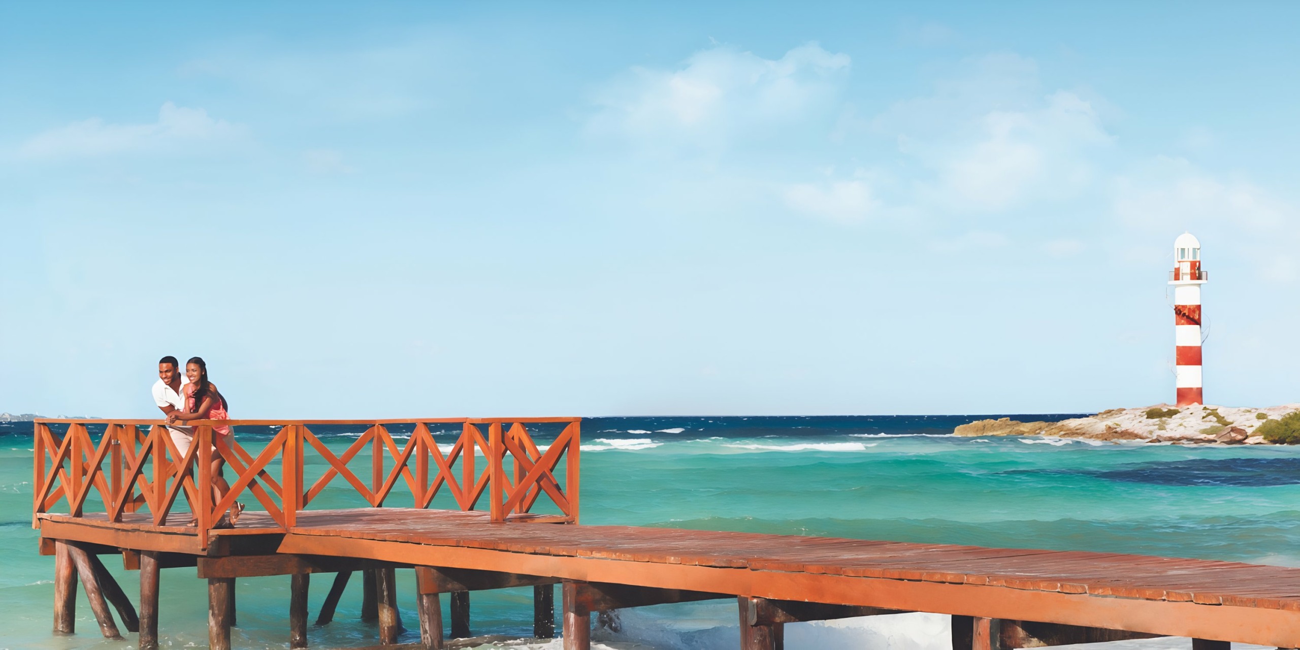 Couple embracing on a wooden pier near a lighthouse with the ocean in the background at Hyatt Ziva Cancun.