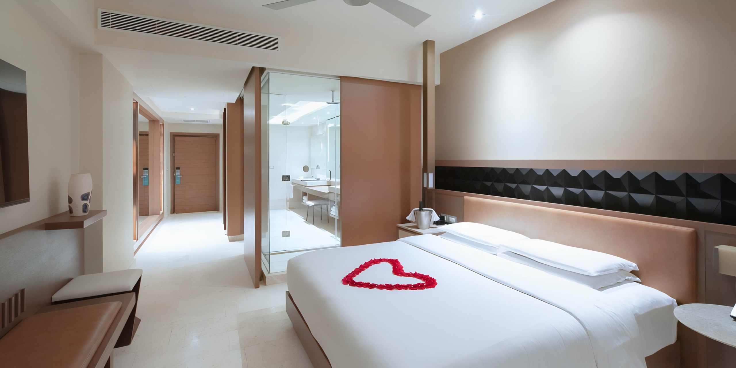 A neat Hyatt Ziva Cancun hotel room with a heart-shaped arrangement of rose petals on the bed, leading to an en-suite bathroom.
