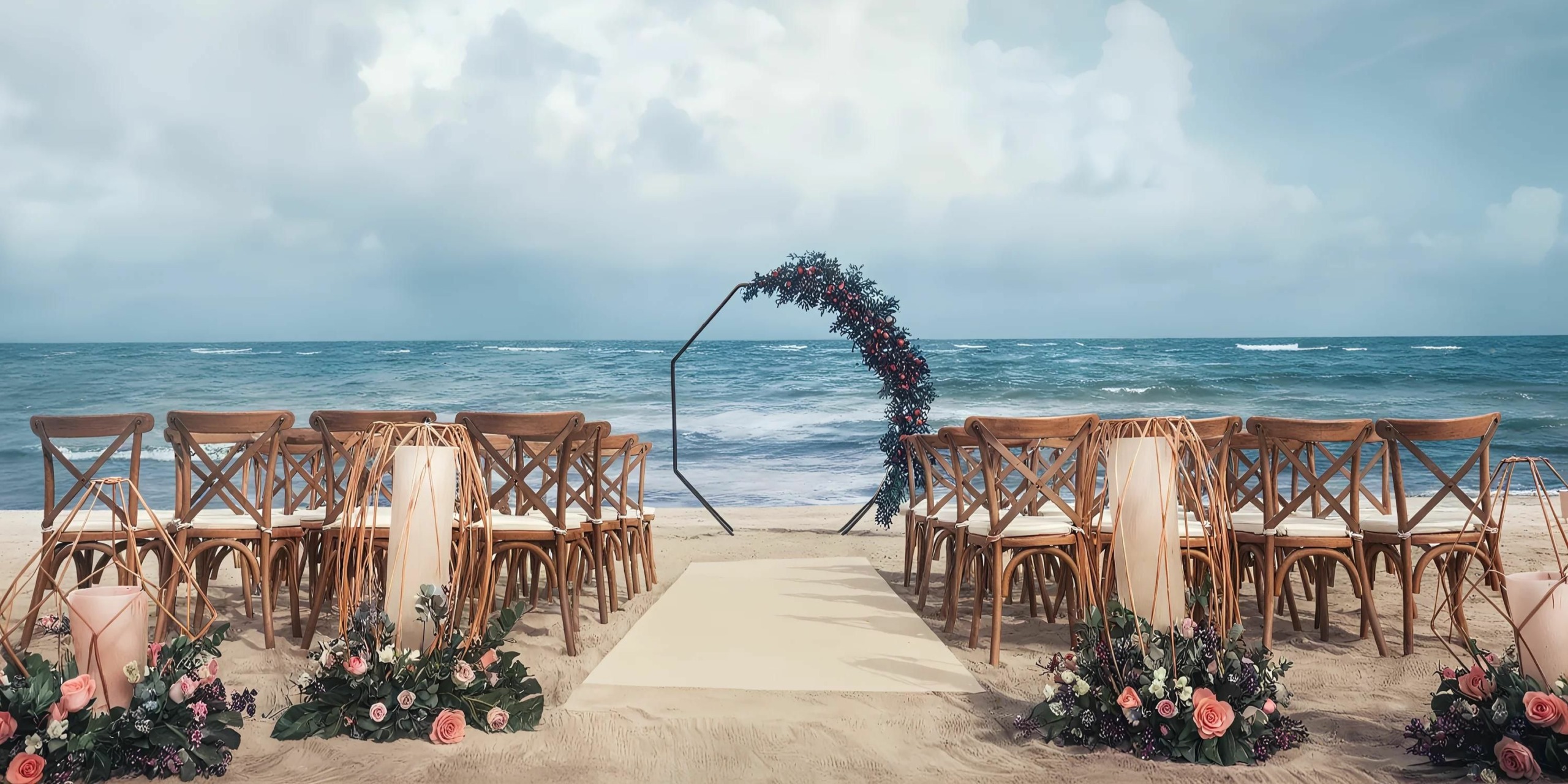 A beachside wedding ceremony setup with wooden chairs arranged in rows, floral decorations, and a circular flower arch facing the ocean.