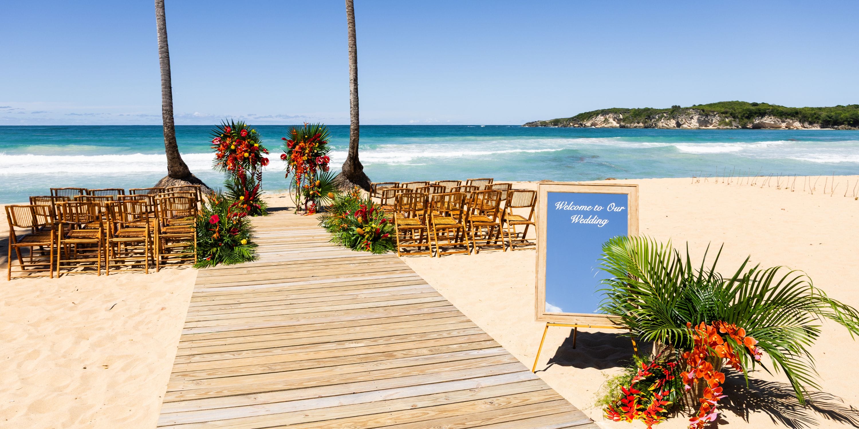 Wooden walkway to a destination wedding at Dreams Macao Beach, lined with chairs, flowers, and welcome sign.