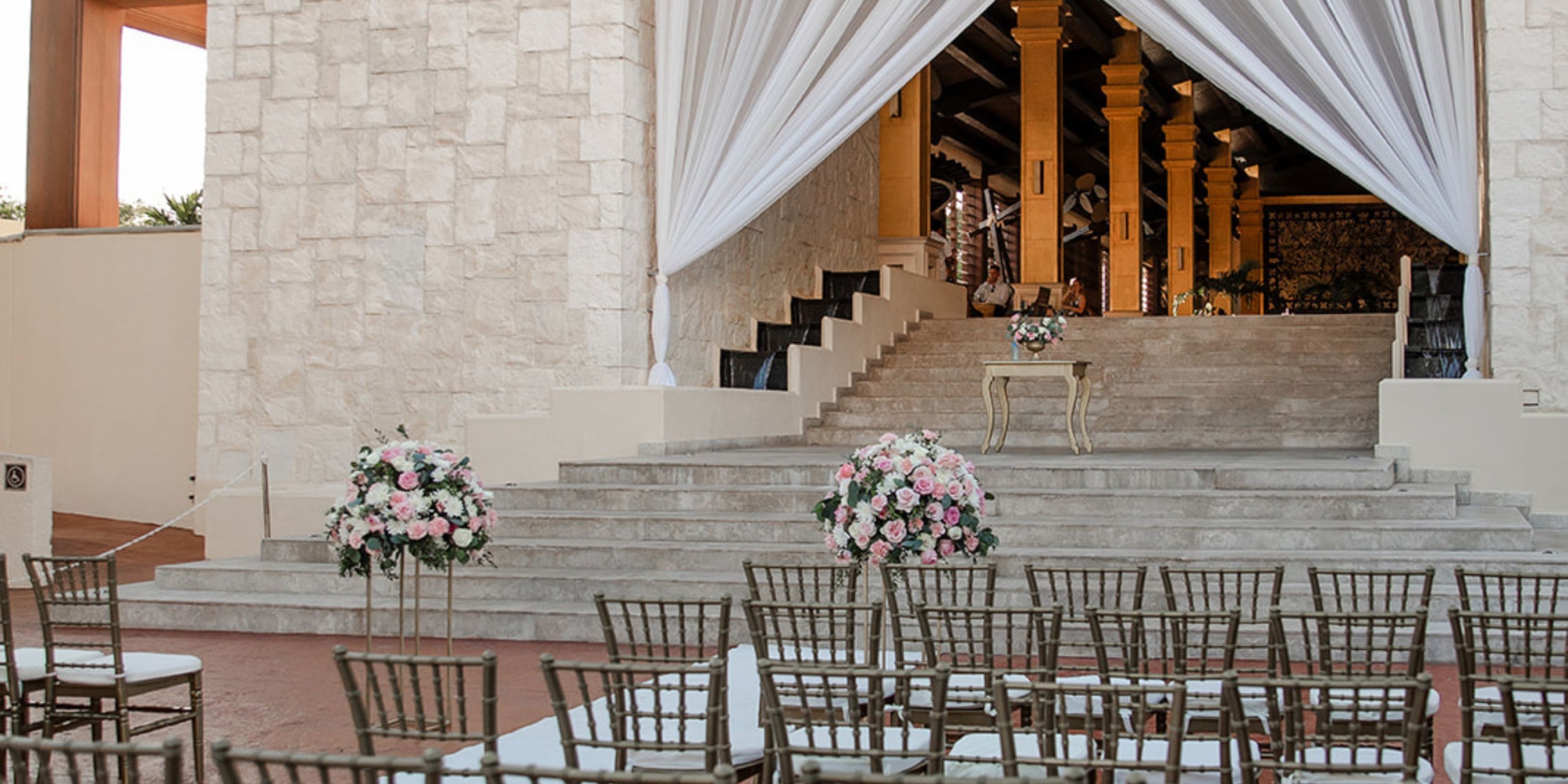 The outdoor wedding setup at Dreams Riviera Cancun features elegantly arranged chairs and beautiful florals, all facing the picturesque stone steps. This setting makes it an ideal location for a destination wedding.