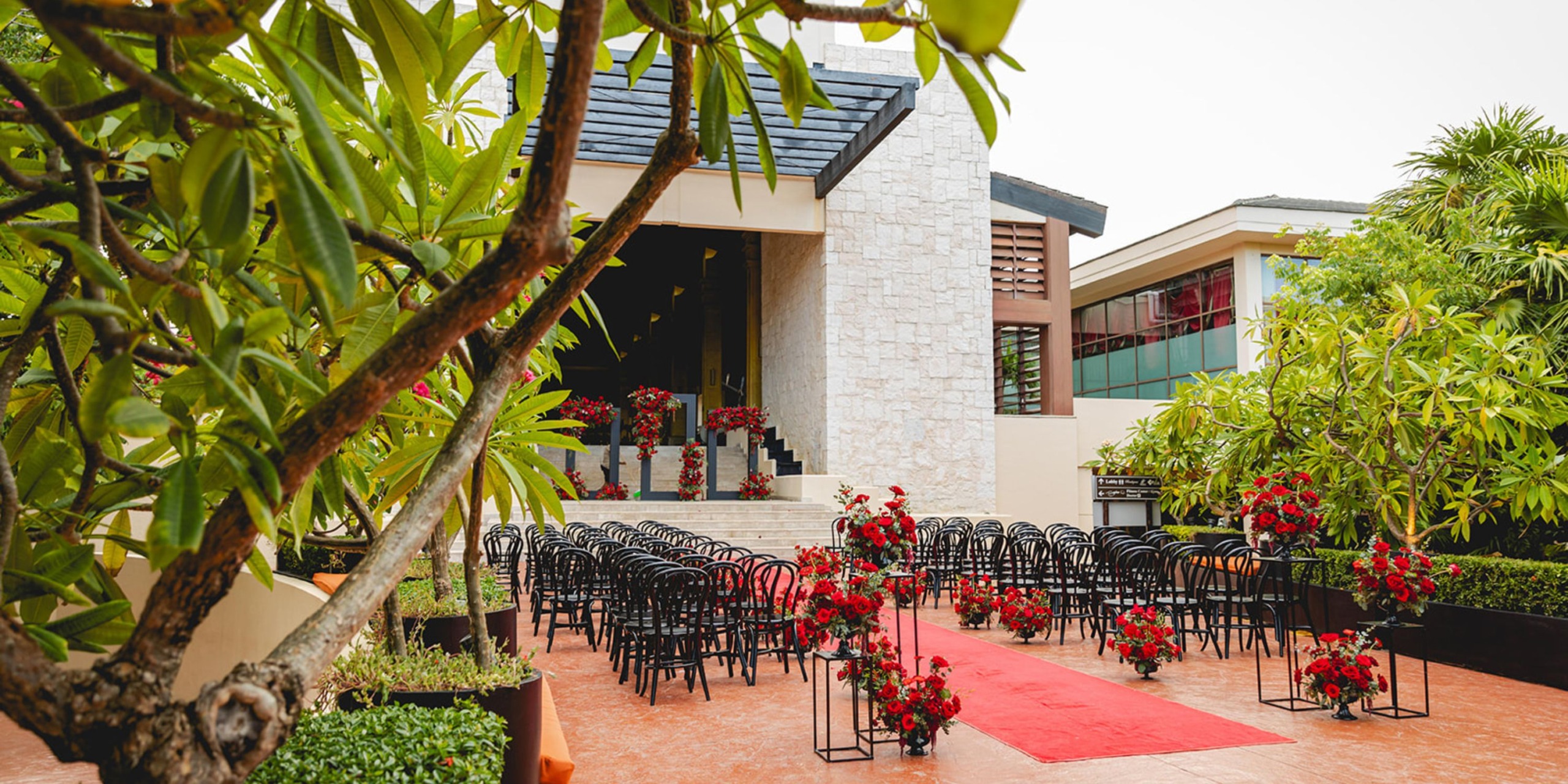 Dreams Riviera Cancun offers a stunning setting for destination weddings, featuring elegant black chairs and vibrant red floral decorations for outdoor ceremonies.