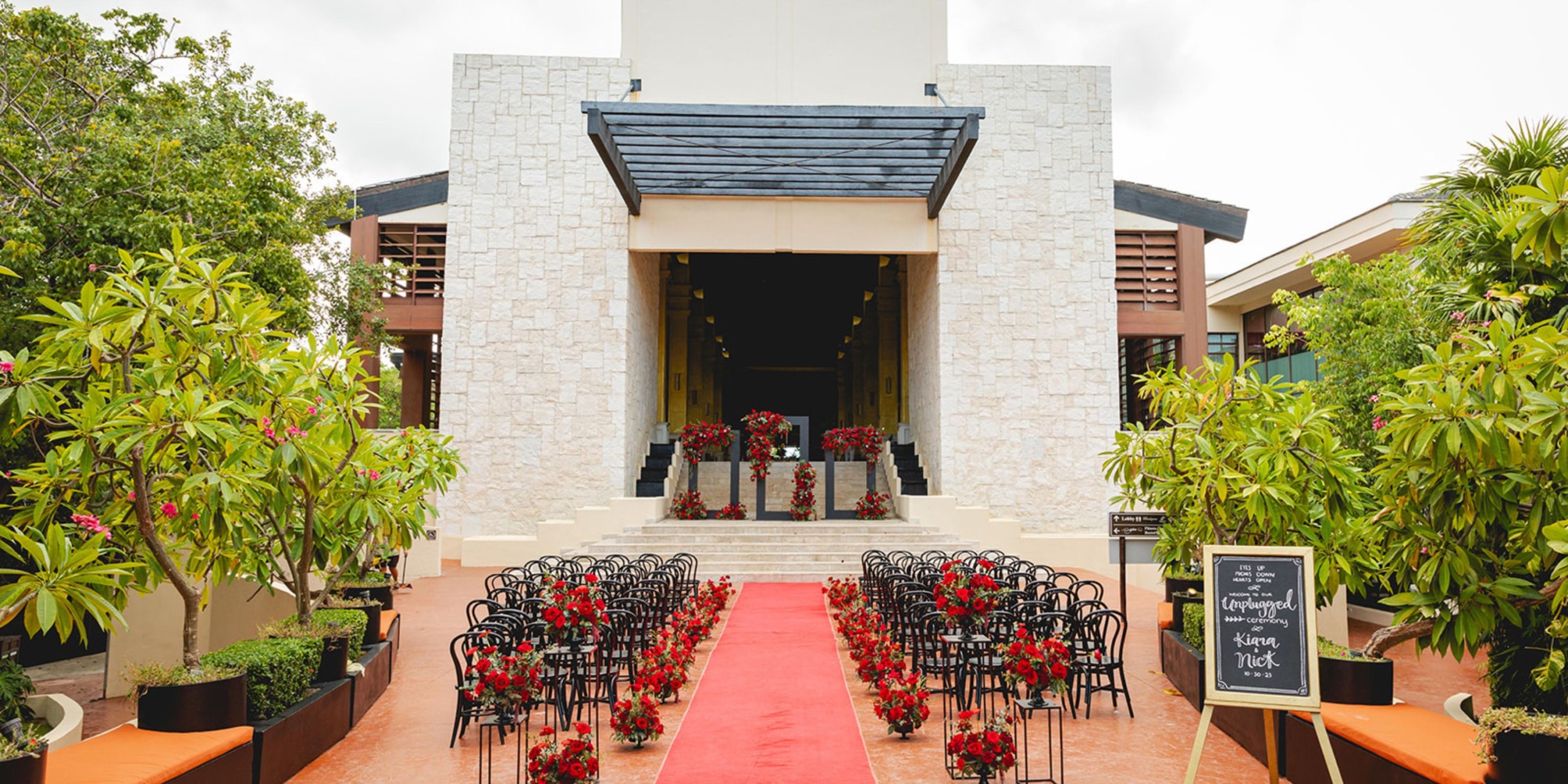 Dreams Riviera Cancun: A destination wedding with a red carpet aisle, elegant black chairs, and exquisite floral arrangements.