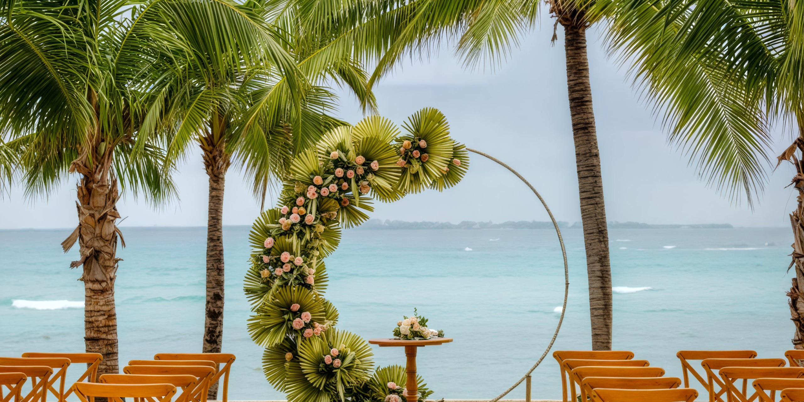 A beautiful destination wedding setup on a tropical beach, featuring a stunning floral arch and rows of empty chairs awaiting guests.