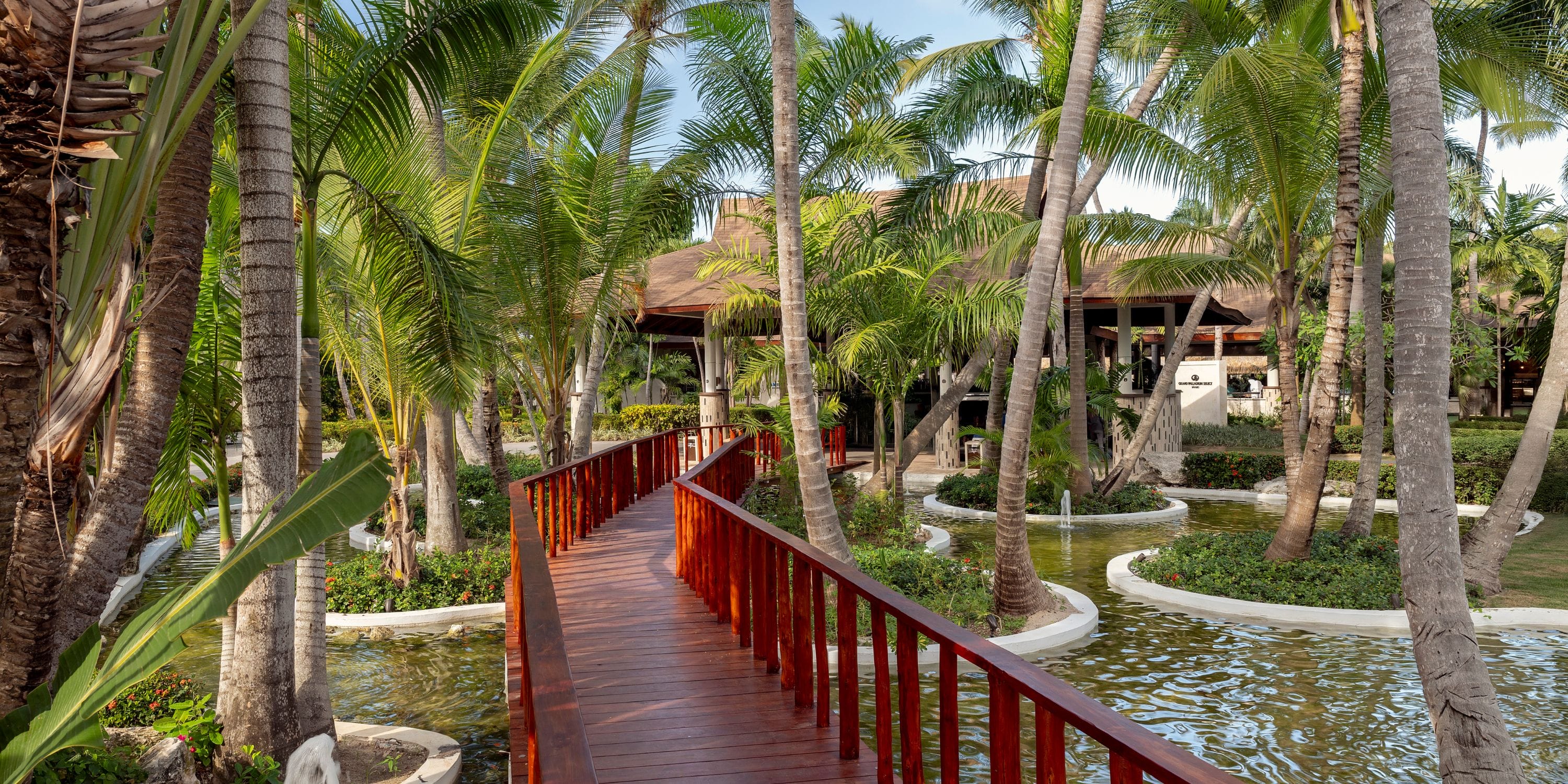 A wooden bridge leads to Grand Palladium Bavaro, a romantic destination wedding spot amid palm trees.