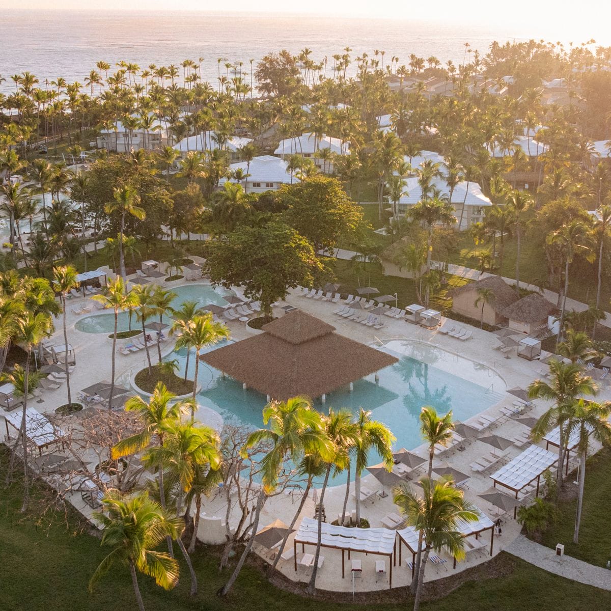 Aerial view of Grand Palladium Bavaro’s pool, palm trees, and ocean at sunset, ideal for a wedding.