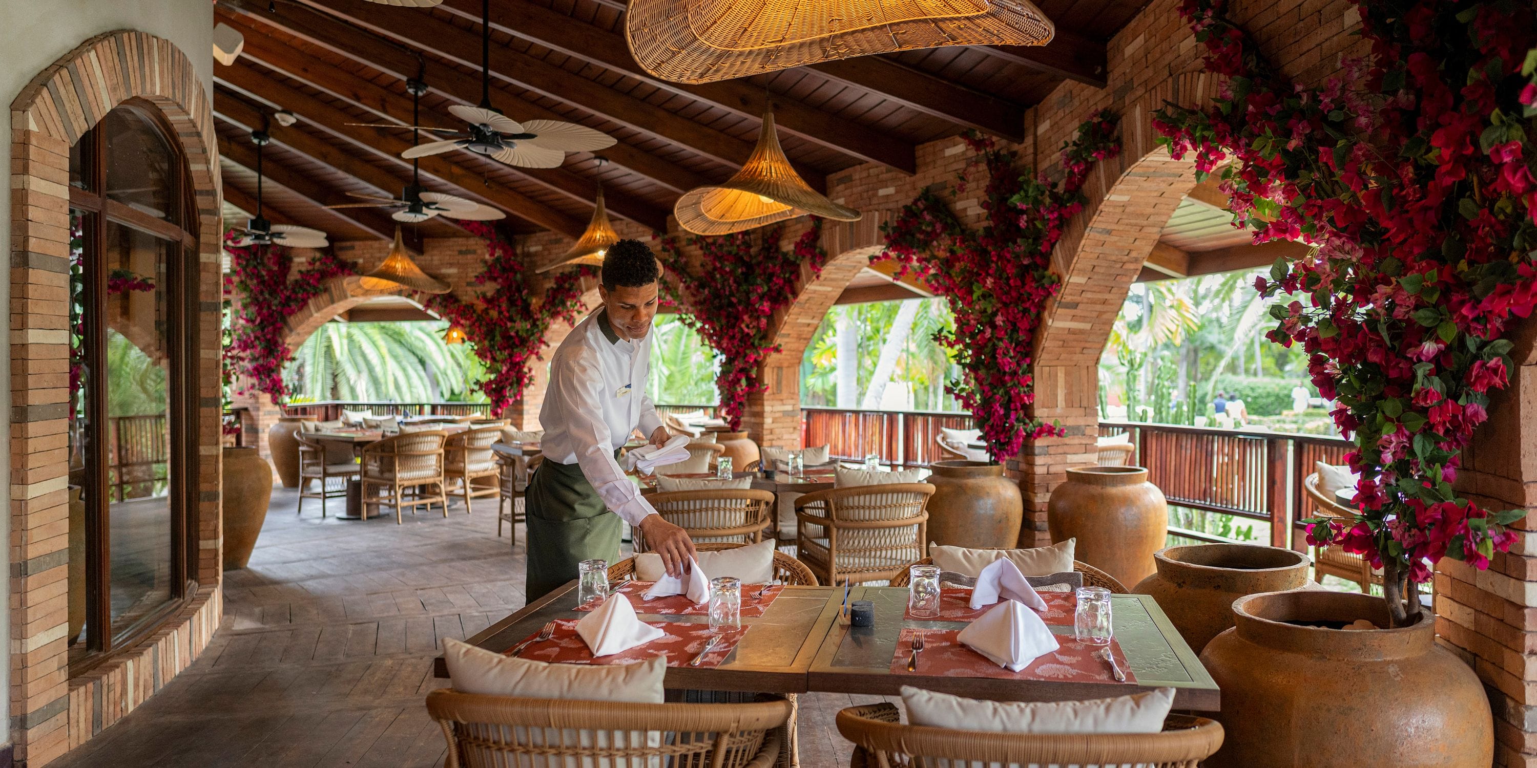 A waiter prepares a table for a destination wedding at Grand Palladium Bavaro's brick-arched patio.