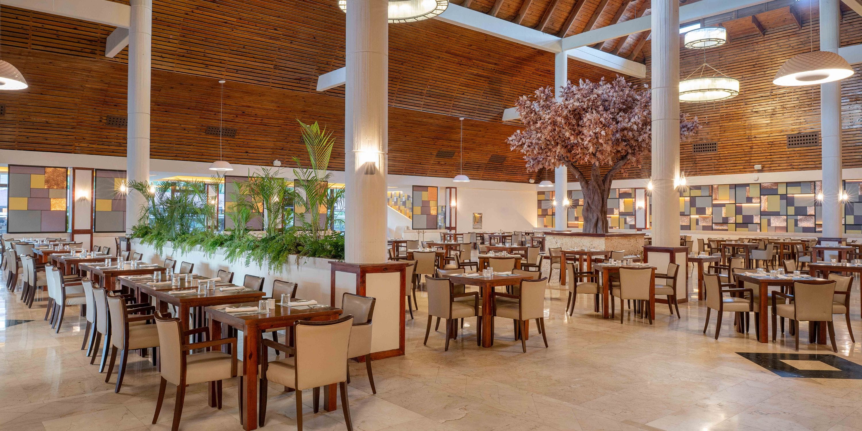 Grand Palladium Bavaro: spacious wedding venue with wooden tables, beige chairs, and a central tree.