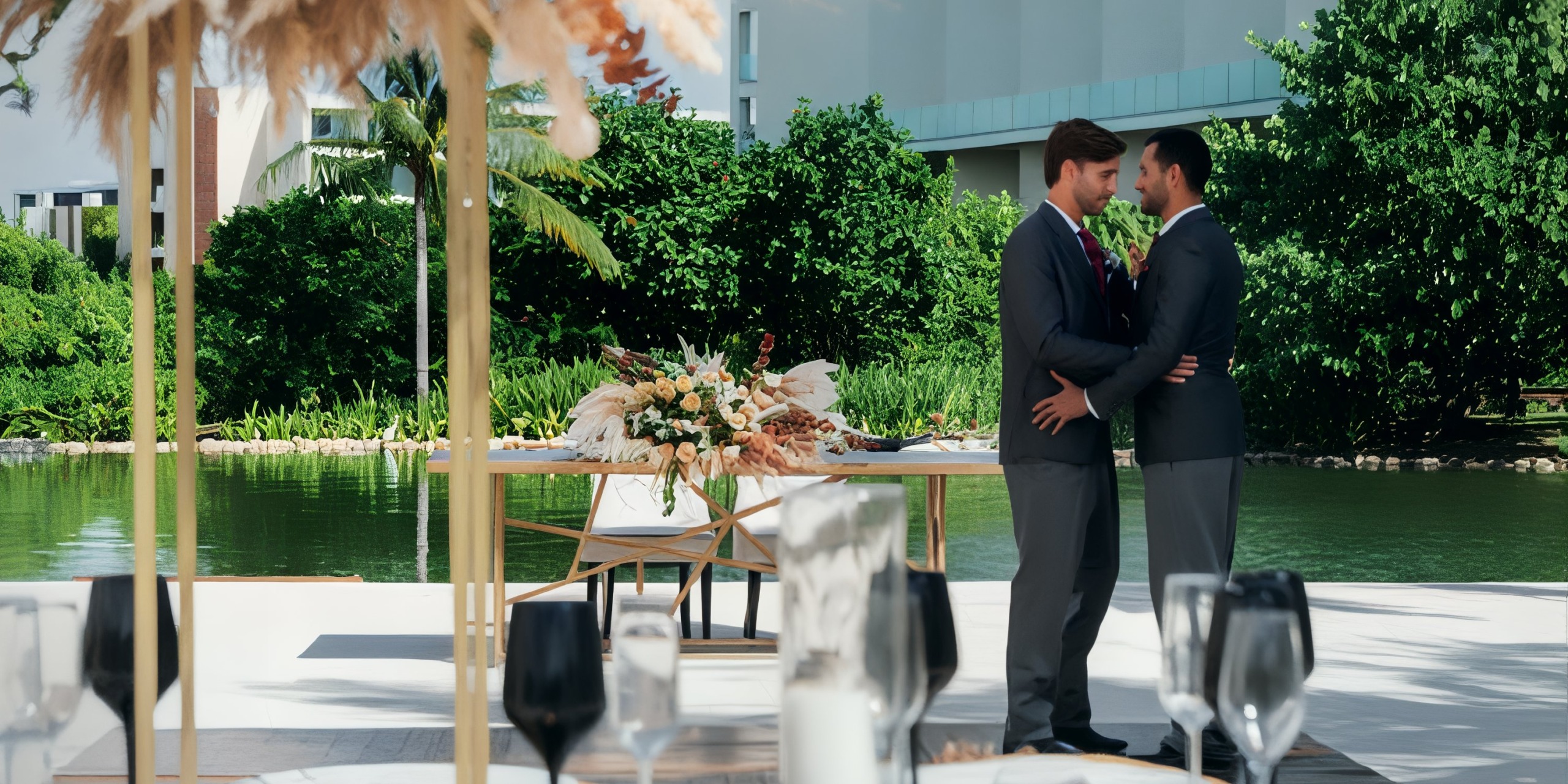 Two men share an embrace near a beautifully decorated table by the pond at Grand Palladium Costa Mujeres, creating a picturesque moment that captures the essence of a destination wedding.