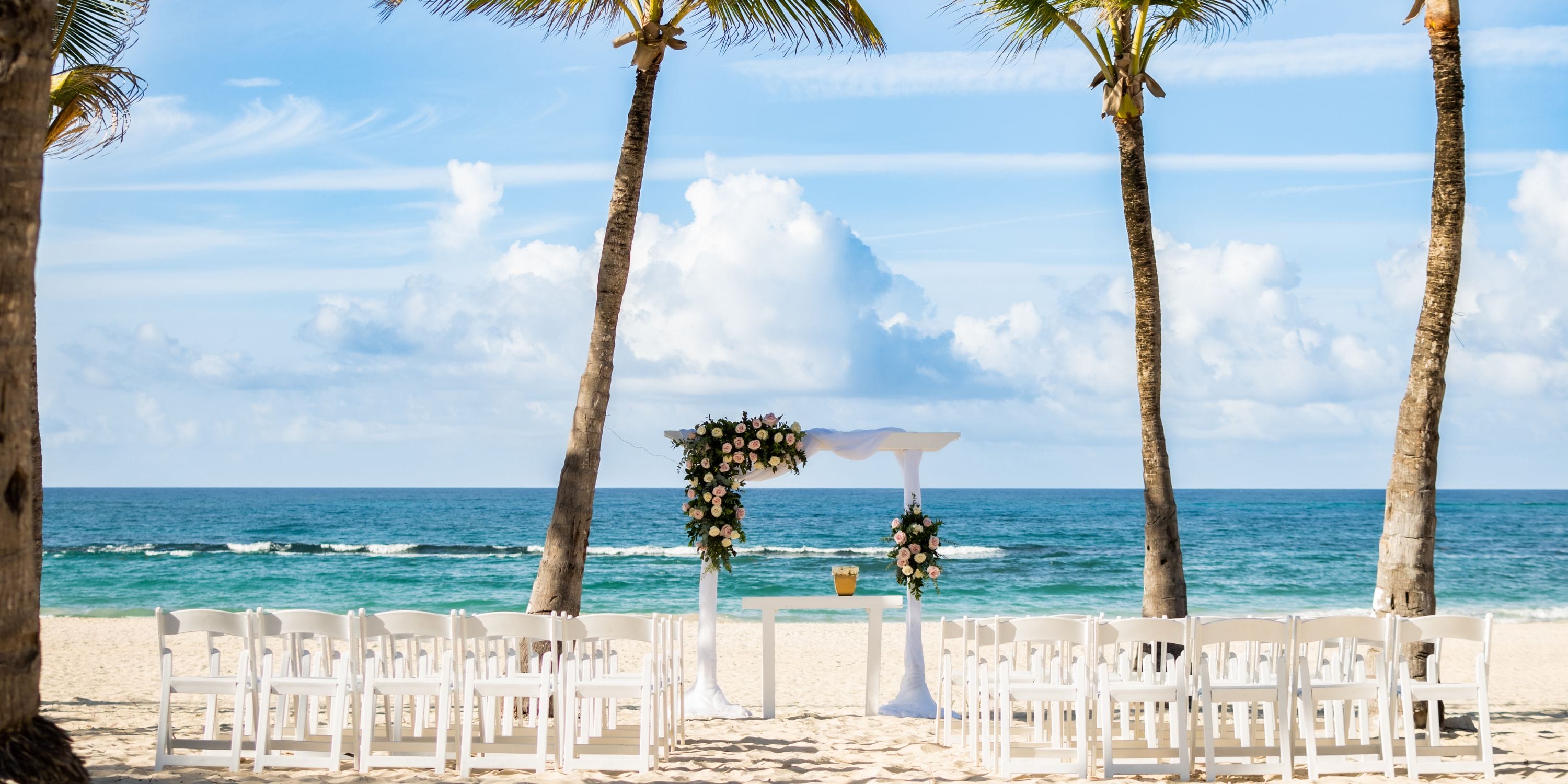White chairs and a floral arch ready for a destination wedding on the beach at Hard Rock Punta Cana.