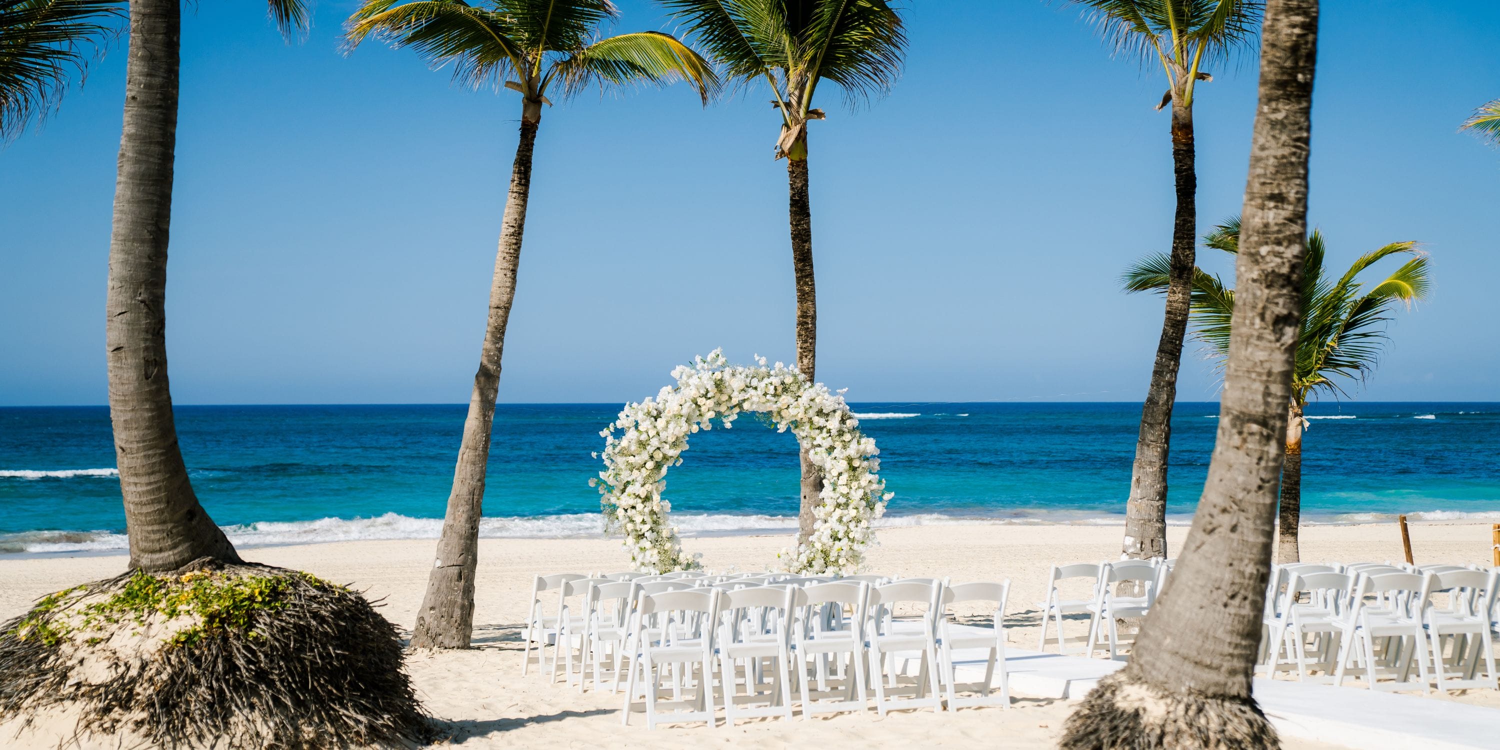 White chairs and a floral arch arranged on sandy beach for a destination wedding at Hard Rock Punta Cana.