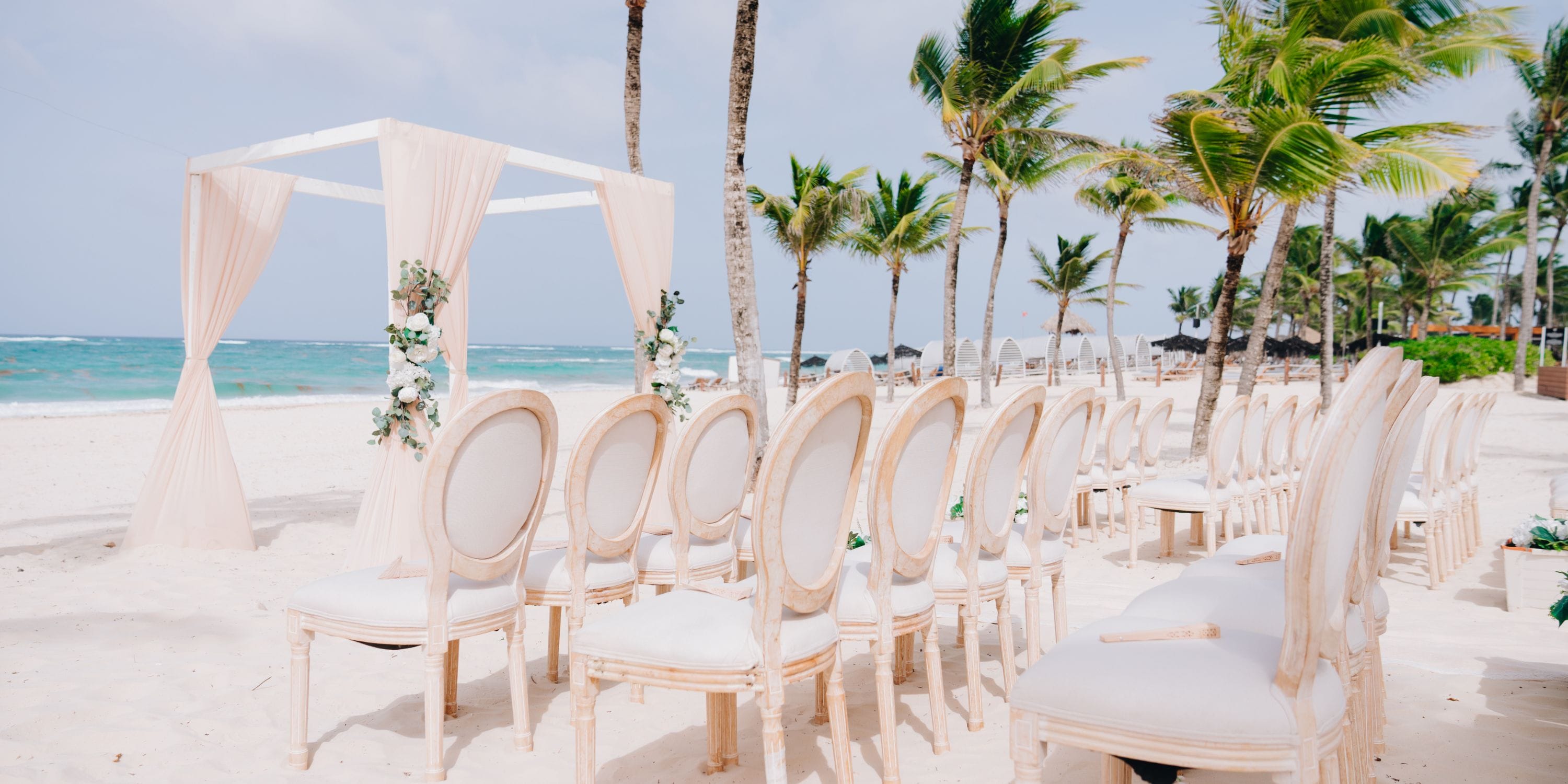 White chairs and an altar are arranged on the sand for a destination wedding at Hard Rock Punta Cana.