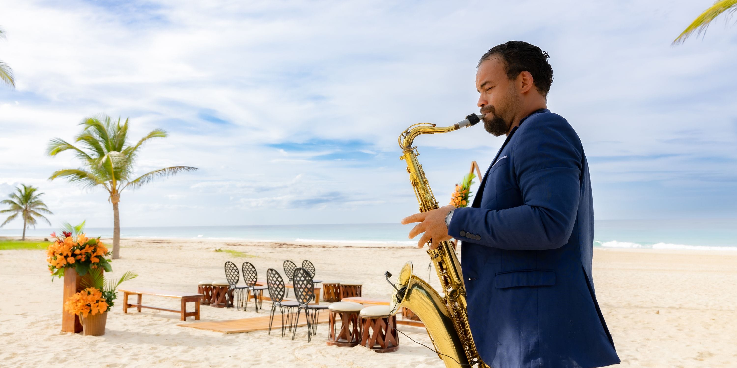 Man in blue suit plays saxophone on sandy beach during a destination wedding at Hard Rock Punta Cana.