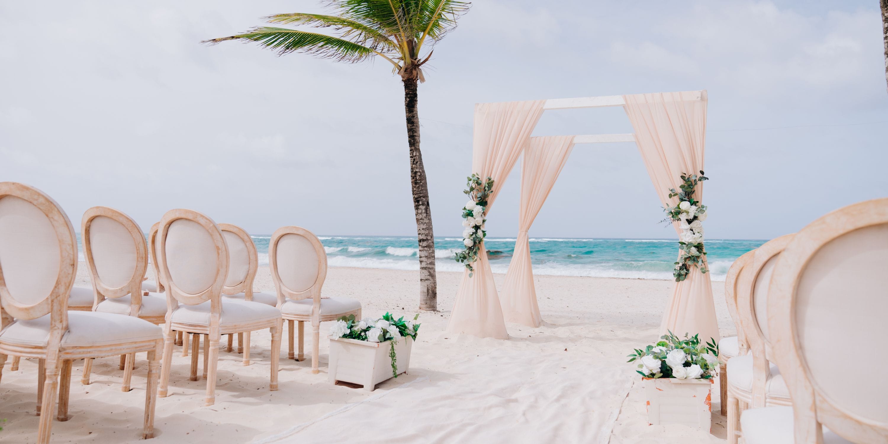 Destination wedding at Hard Rock Punta Cana: beachside ceremony with chairs, floral accents, and ocean arch.