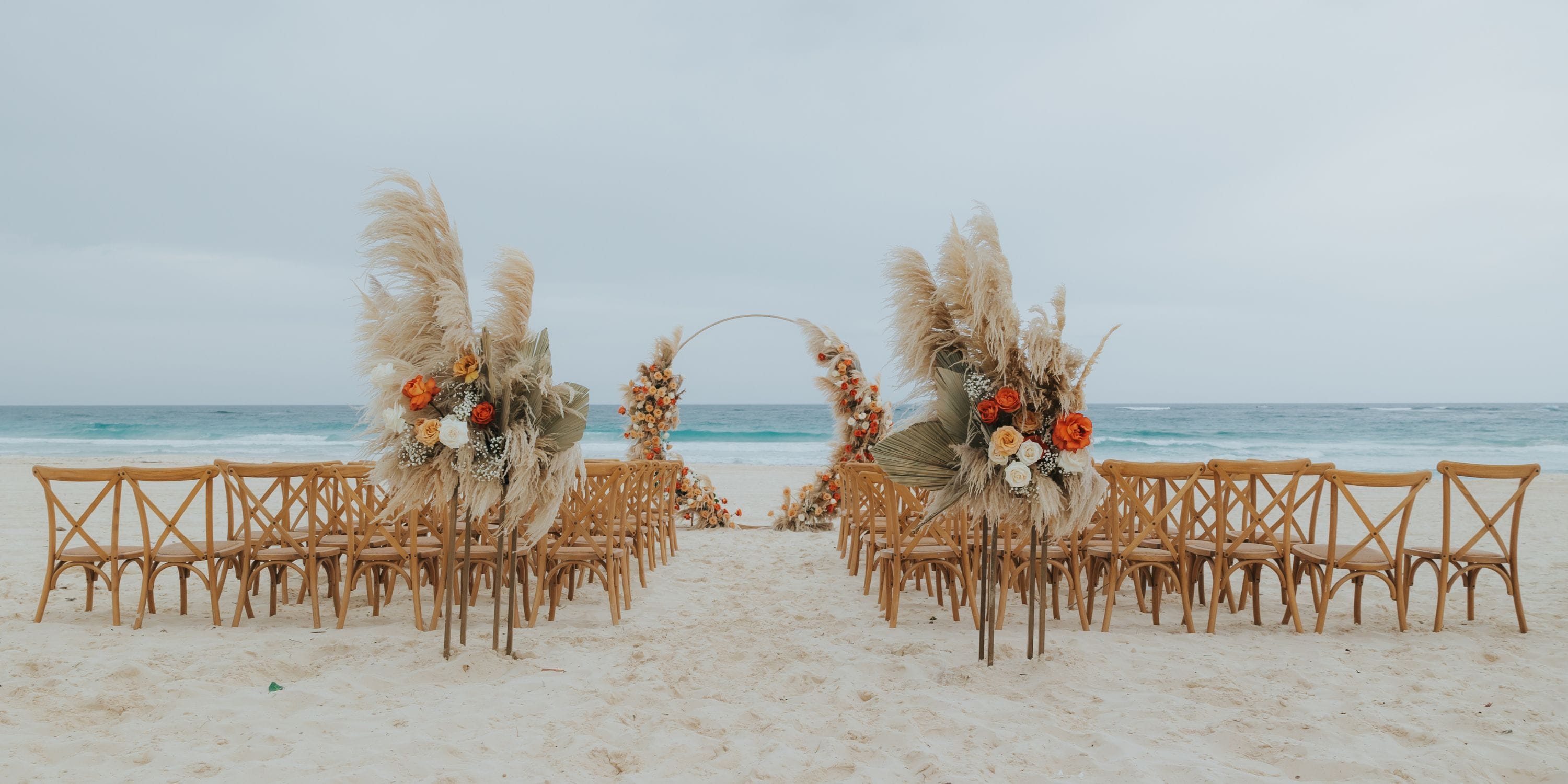 Destination wedding setup at Hard Rock Punta Cana featuring wooden chairs and a floral arch on the beach.