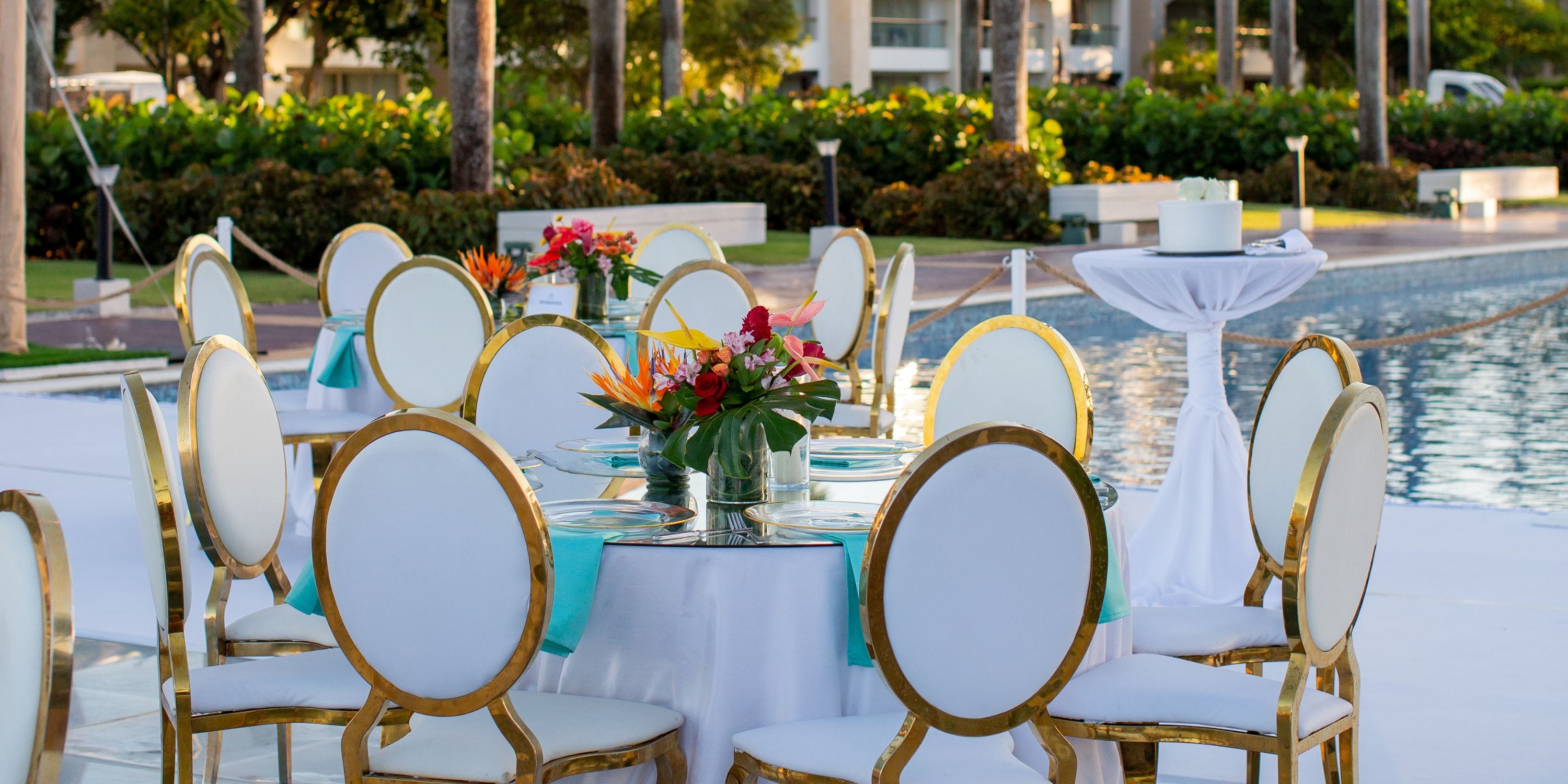Hard Rock Punta Cana's outdoor dining set for a destination wedding, with white chairs and floral centerpieces by the pool.