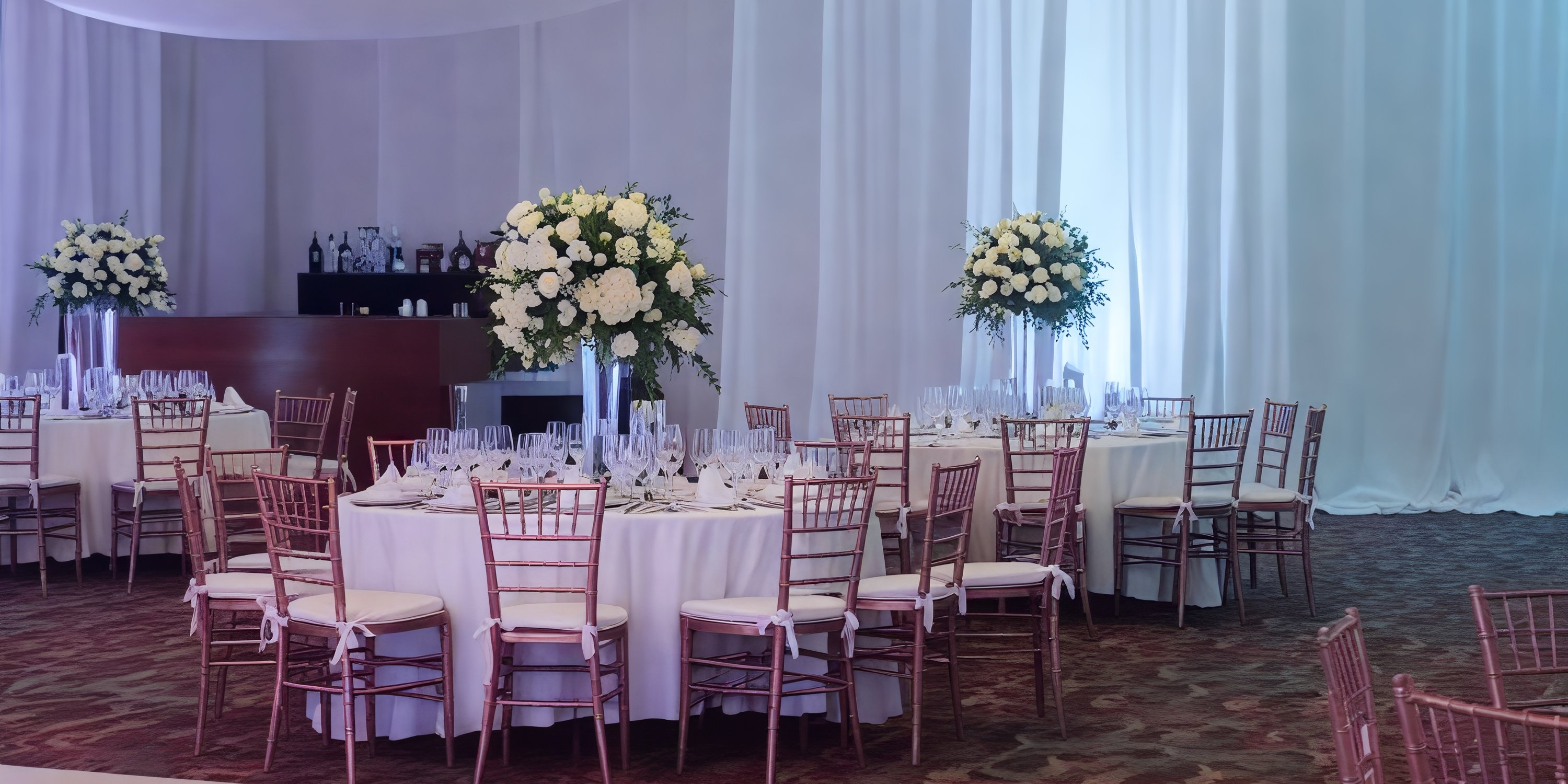 An elegant ballroom set for a destination wedding, featuring round tables adorned with floral centerpieces and accented by graceful white drapery.