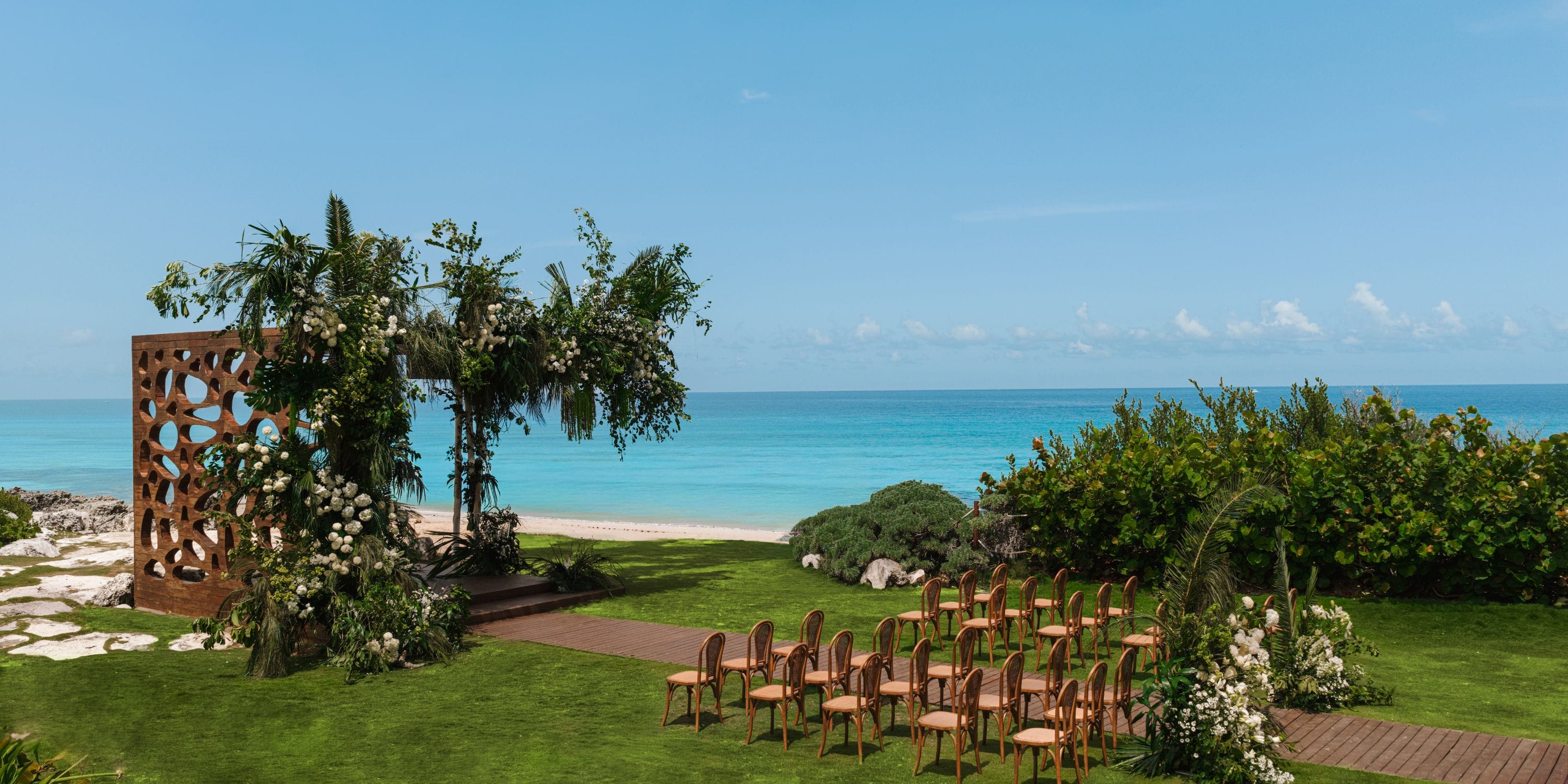 Rows of chairs set up for a destination wedding face an altar on the lawn by the ocean at Hyatt Ziva Cancun.