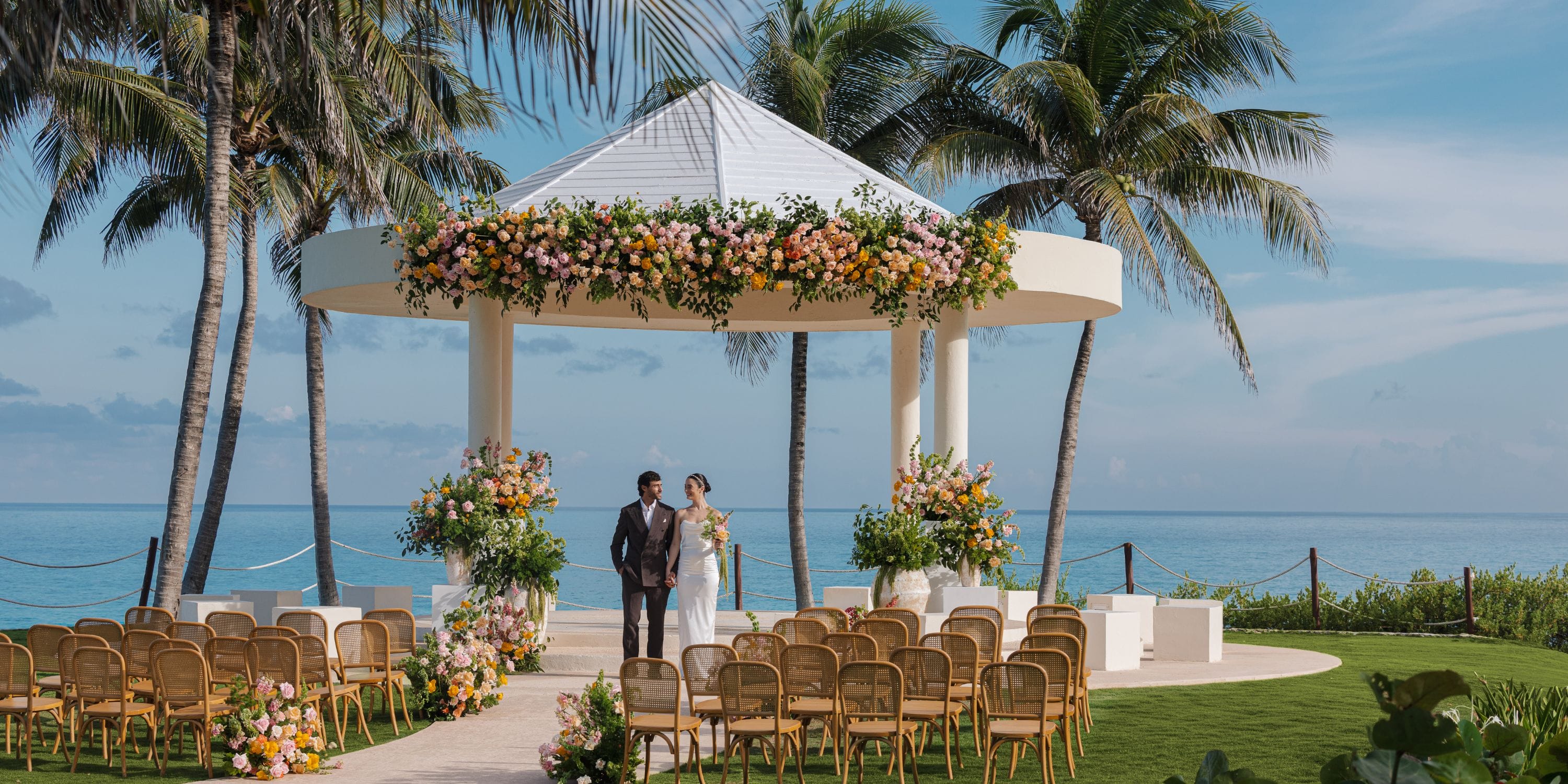 Bride and groom at their destination wedding at Hyatt Ziva Cancun, under a floral gazebo by the ocean.