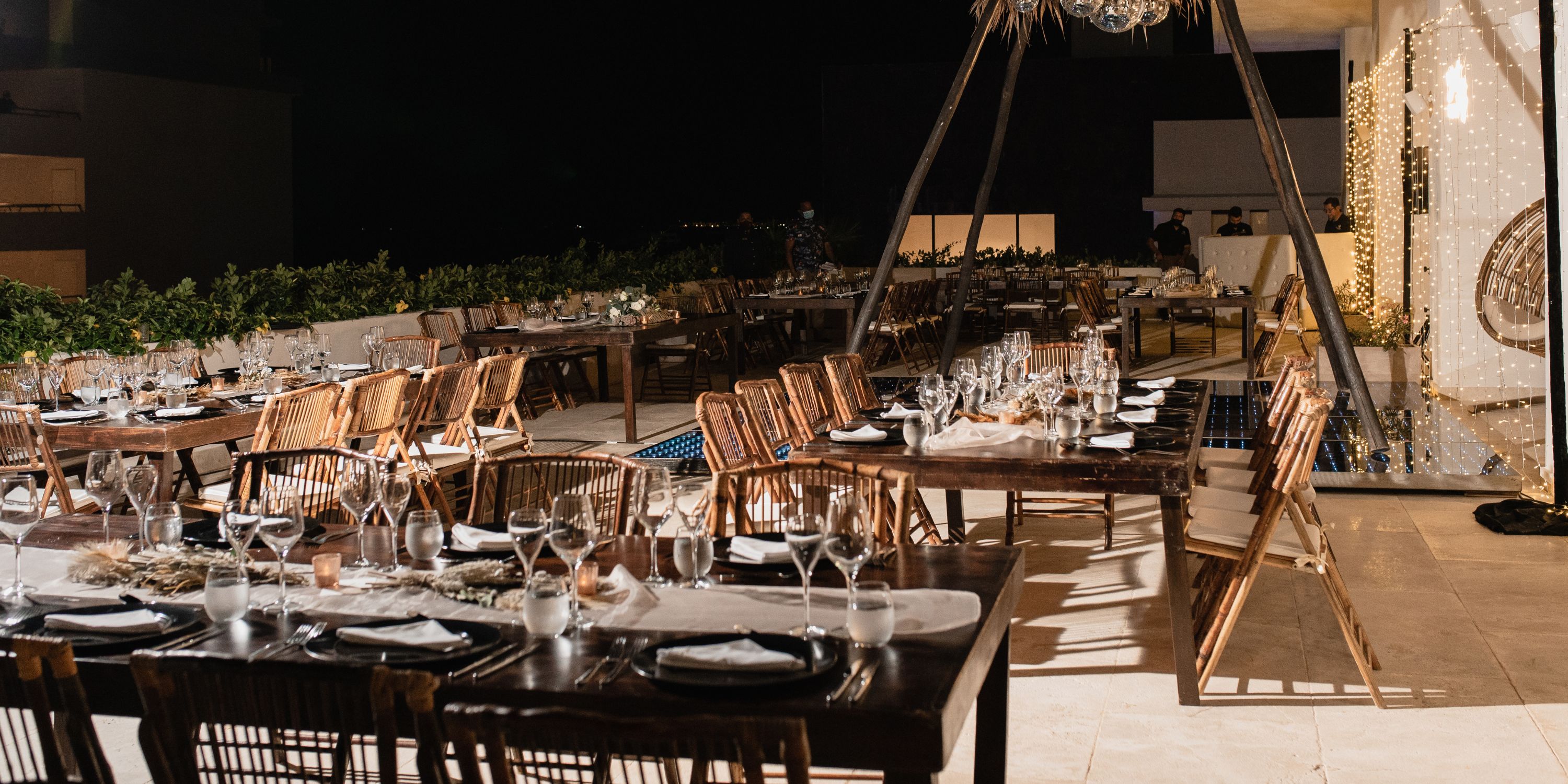 Majestic Elegance Costa Mujeres destination wedding setup with wooden tables, chairs, plates, and glassware at night.