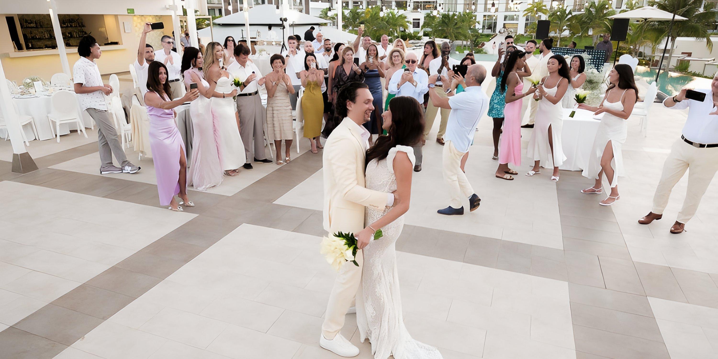 The bride and groom share a dance at their destination wedding outdoors as guests watch and take photos.