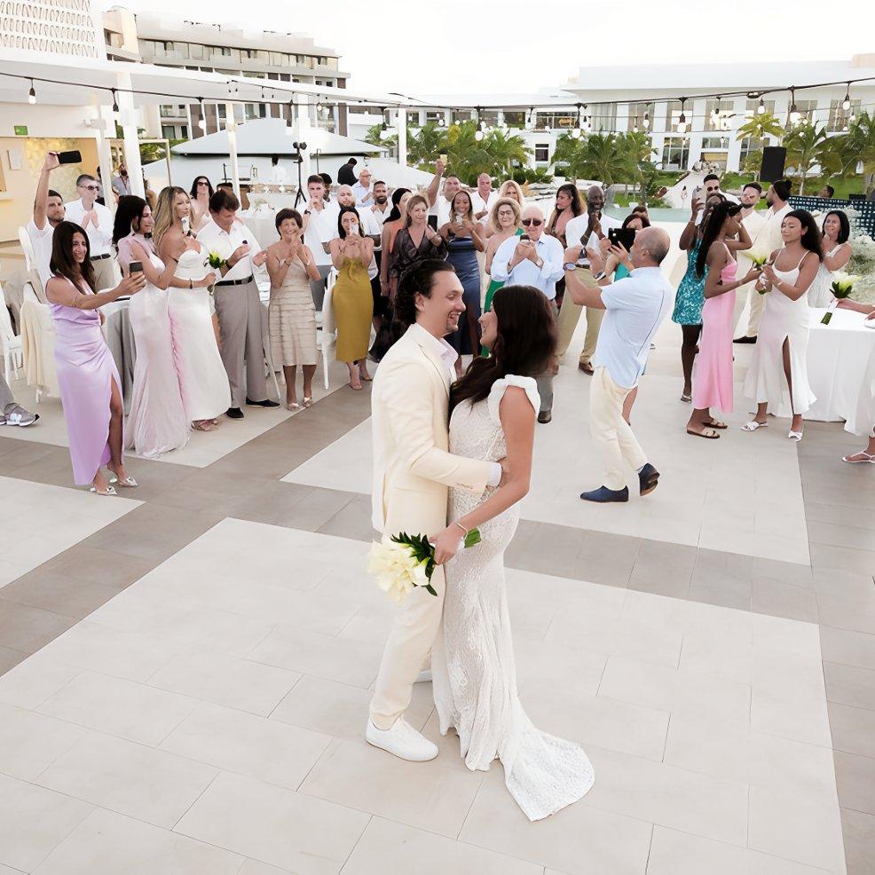 A bride and groom share a dance at their destination wedding as guests look on and capture photos outdoors.