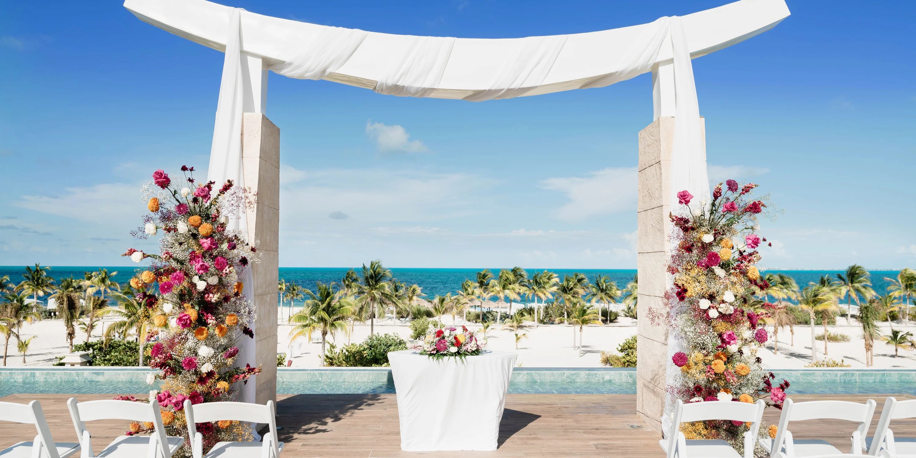 Destination wedding altar at Majestic Elegance Costa Mujeres, florals and ocean backdrop beneath blue sky.
