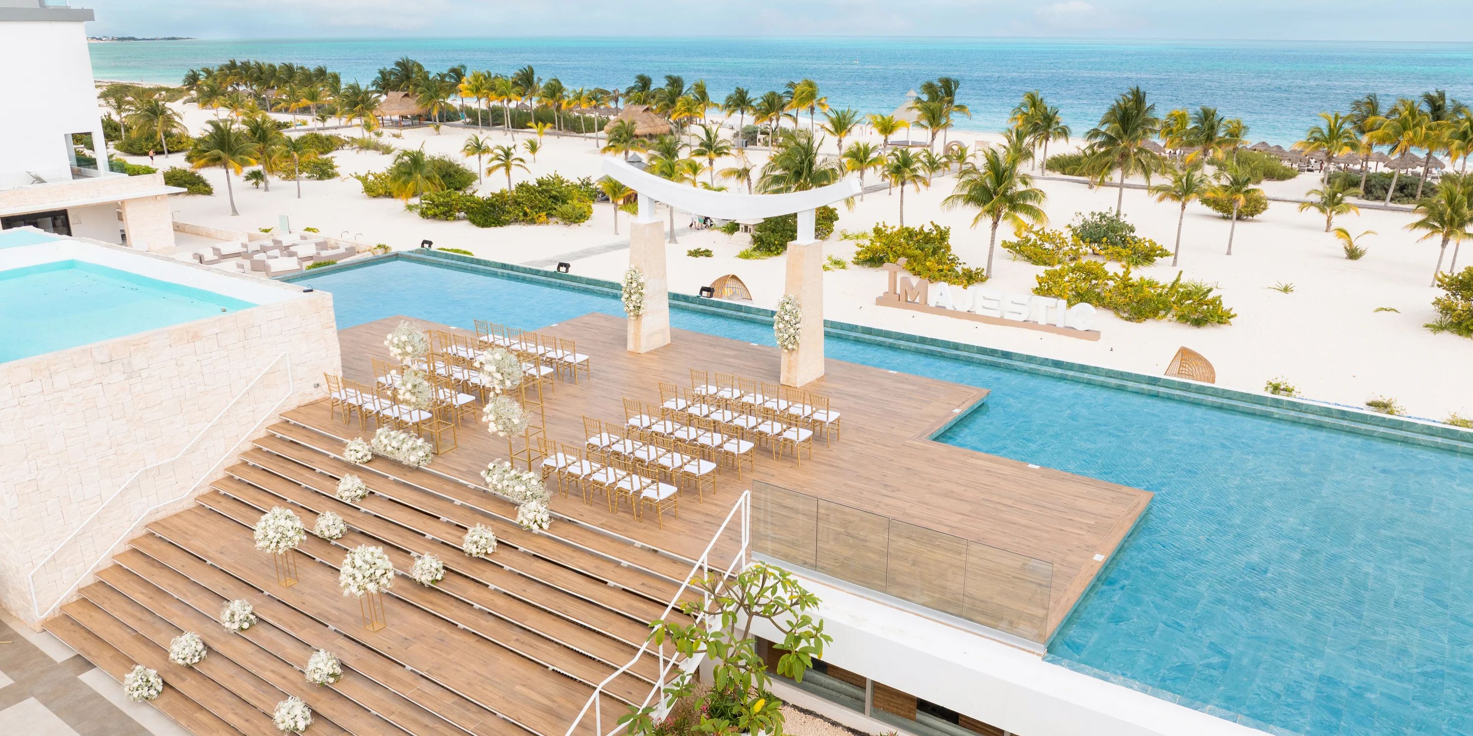 Destination wedding ceremony setup at Majestic Elegance Costa Mujeres, chairs line a wooden deck by the pool.