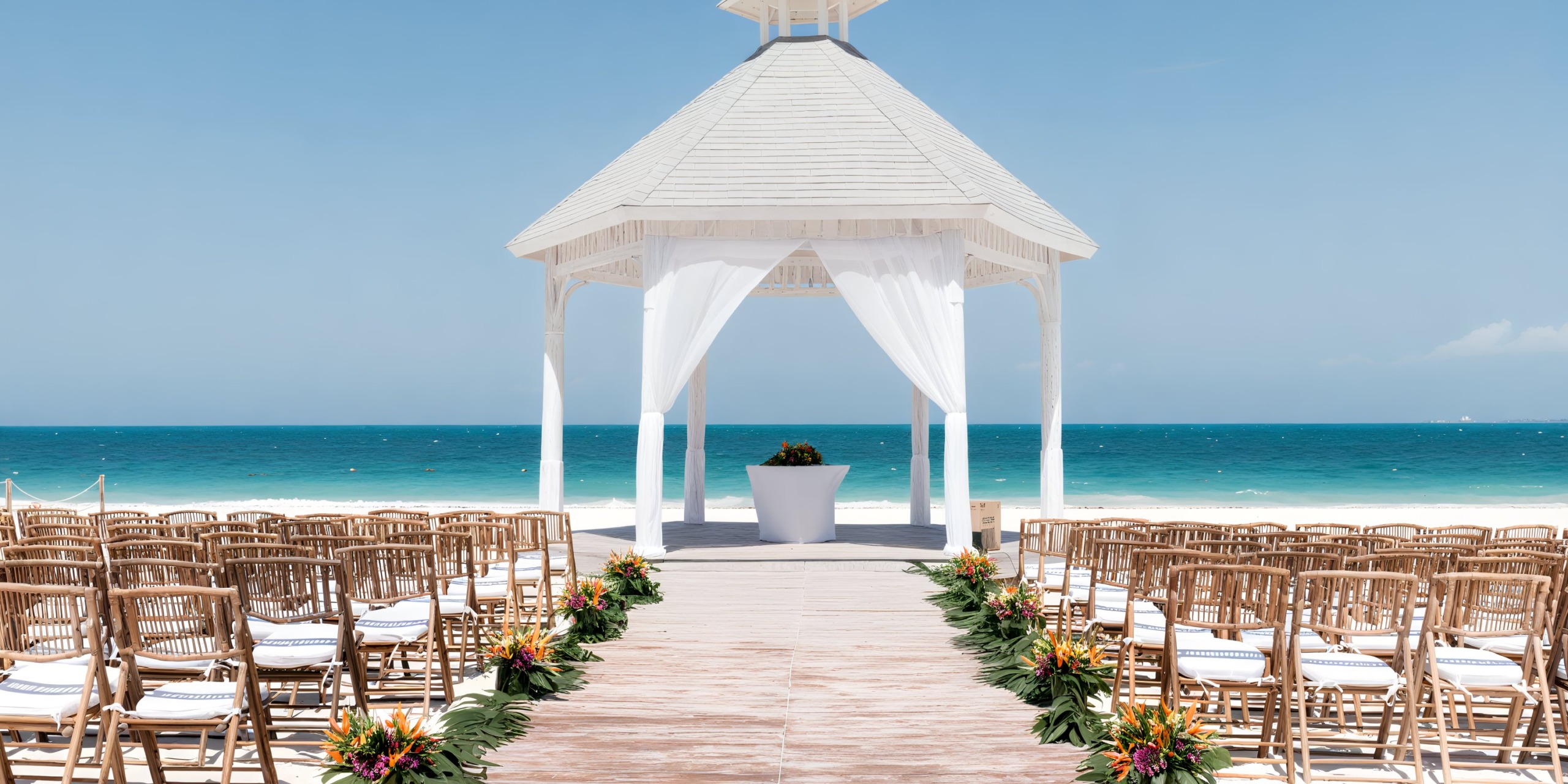 Experience a breathtaking destination wedding at Majestic Elegance Costa Mujeres, featuring a stunning beach setup. Imagine exchanging vows on a floral-lined aisle leading to a white gazebo, all set against the backdrop of the mesmerizing ocean.