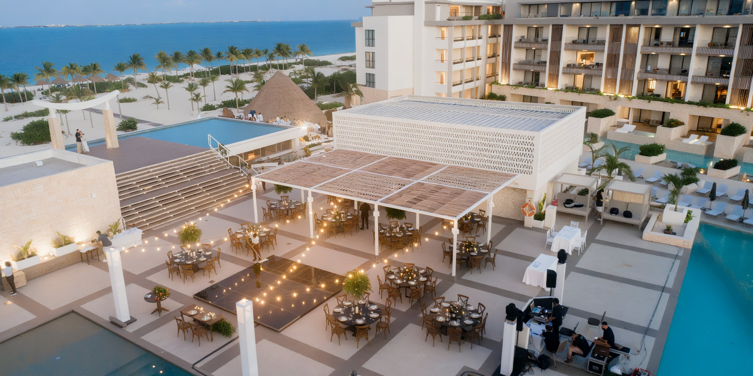 Wedding rooftop event setup by a pool with elegantly adorned tables and twinkling lights at the Majestic Elegance Costa Mujeres. Perfect for a destination wedding celebration!.