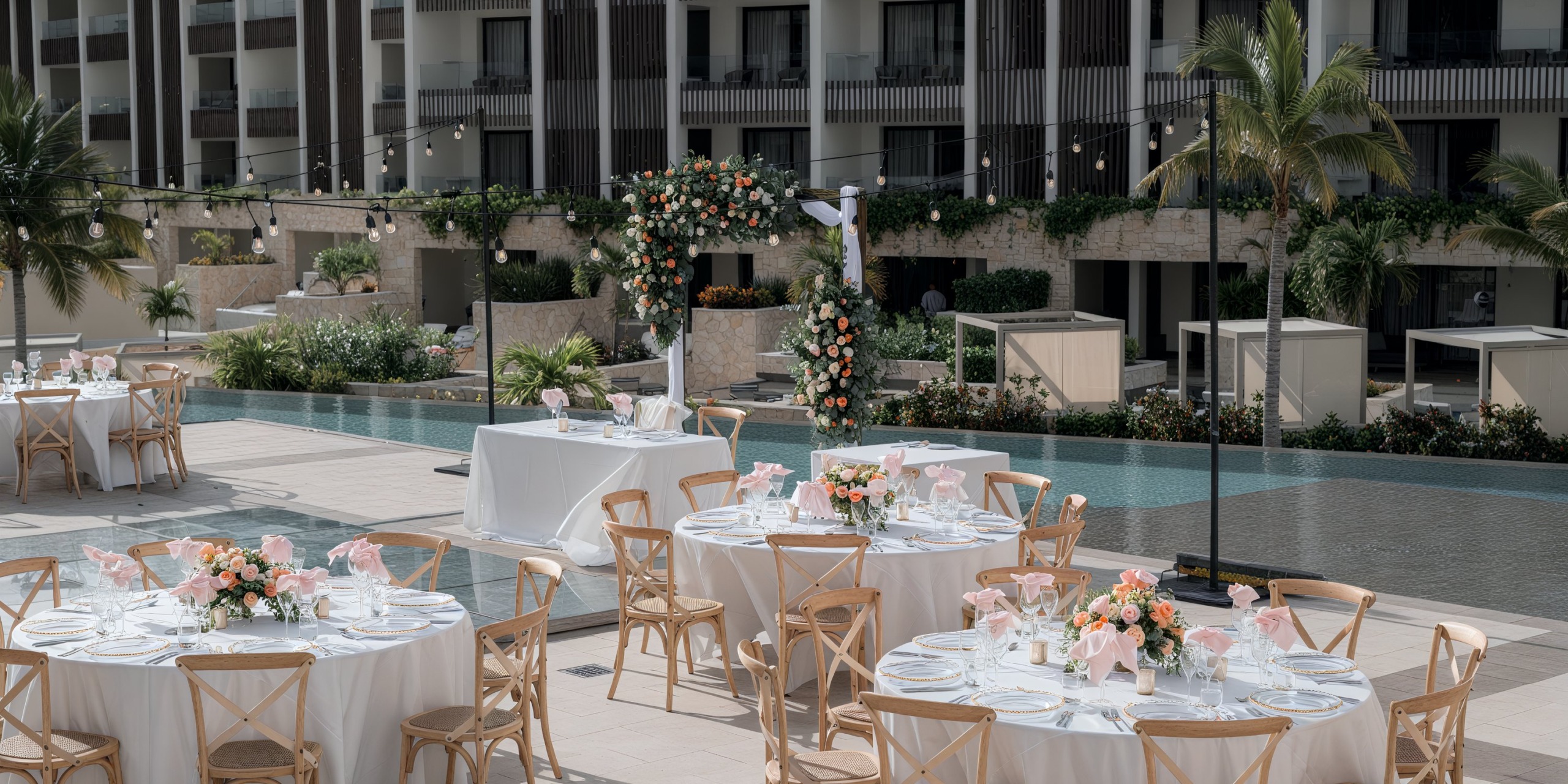 Experience a breathtaking destination wedding at Majestic Elegance Costa Mujeres, featuring outdoor celebrations adorned with round tables, exquisite florals, and stunning views of the pool.